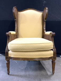 Vintage Wooden Caned Wingback Armchair: Armchair is vintage possibly antique. Piece has caned wingback sides. Chair has gold toned upholstery with patterned detail. Piece has double welting at some edges of upholstery. Armrests have cushion