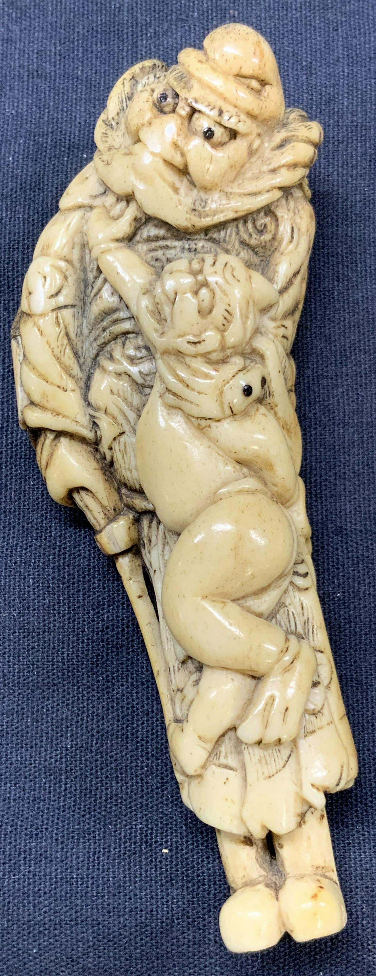 4 Inch Long Carved Bone Netsuke: Carved bone Netsuke, approximately 4 inches long. Possibly depicts a man in intricately carved robes holding a child. No discernible signature. Holes to Netsuke on backside. Moderate Wearing due to ag