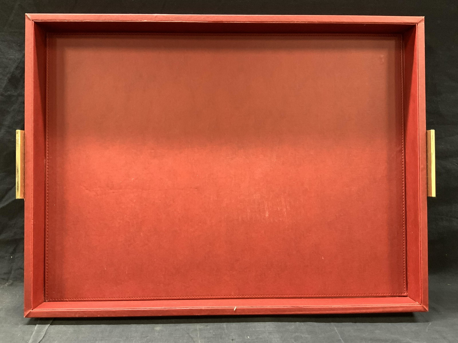 GV Direct MCM Red Table Tray Centerpiece: Marked on underside GV Direct Approximately 24 x 28 inches. Red faux leather lined tray with gold toned metal side handles. Moderate wearing to edge and wearing to leather in center. GV direct tray, c