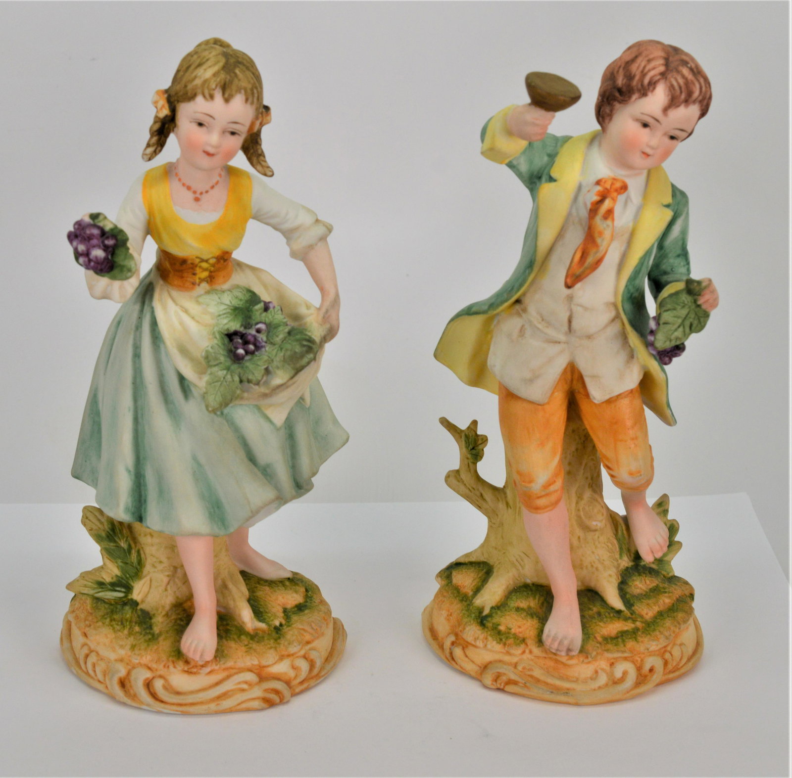Ethan Allen Boy and Girl Porcelain Figurines: Vintage Ethan Allen Porcelain Figurines. Boy and girl with grapes. They stand 8 high and the base is 3.5. There is a chip on the boys tie. Signed and numbered. -NB