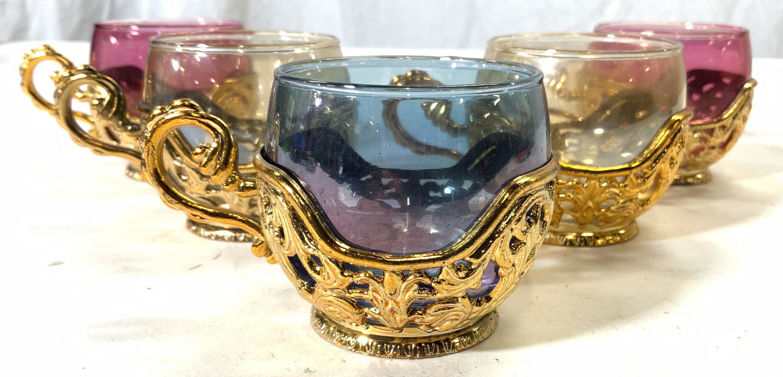 Set 5 Glass Insert Vessels In Ornate Holders ITALY: Holders each read ITALY. Lot includes 5 glass vessels which sit in plastic gold toned ornately detailed holders. Includes 1 blue, 2 pink & 2 orange. Each piece measures approx 3.5 inches deep, 2.5 inc
