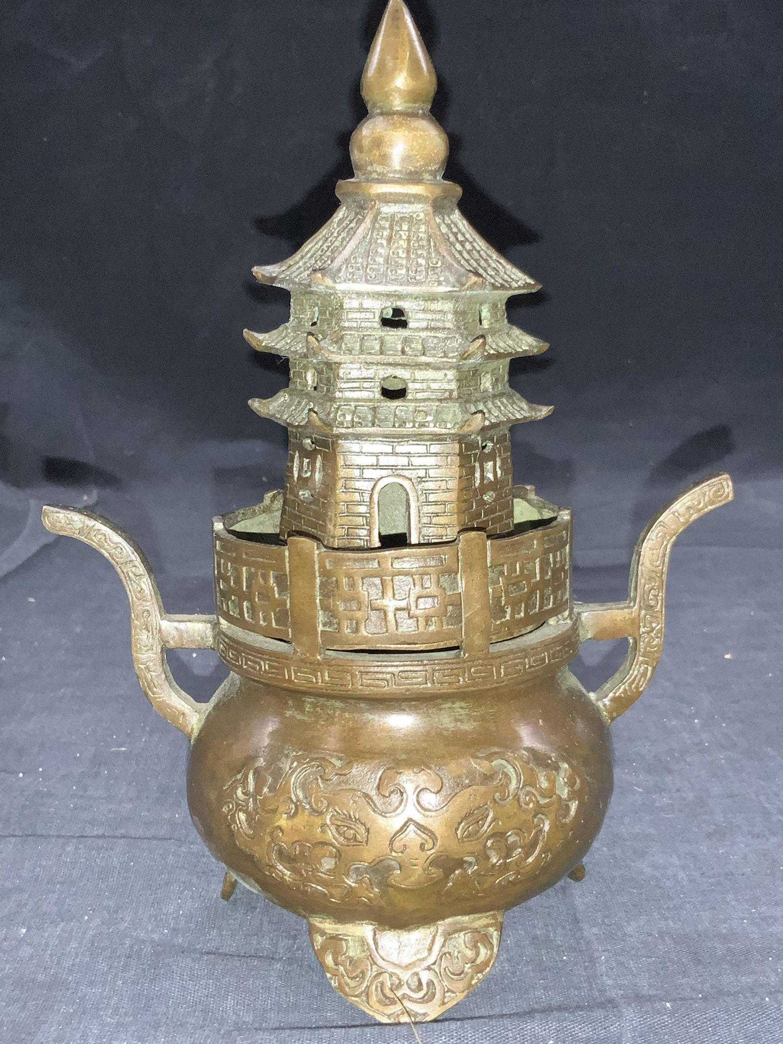 Stamped Asian Pagoda Metal Incenser: Stamped on undersides with Asian characters. Possibly made with patina brass. Two pieces with top resembling a pagoda. Base is resembles a cauldron with side handles sand motif with eyes. Approximatel