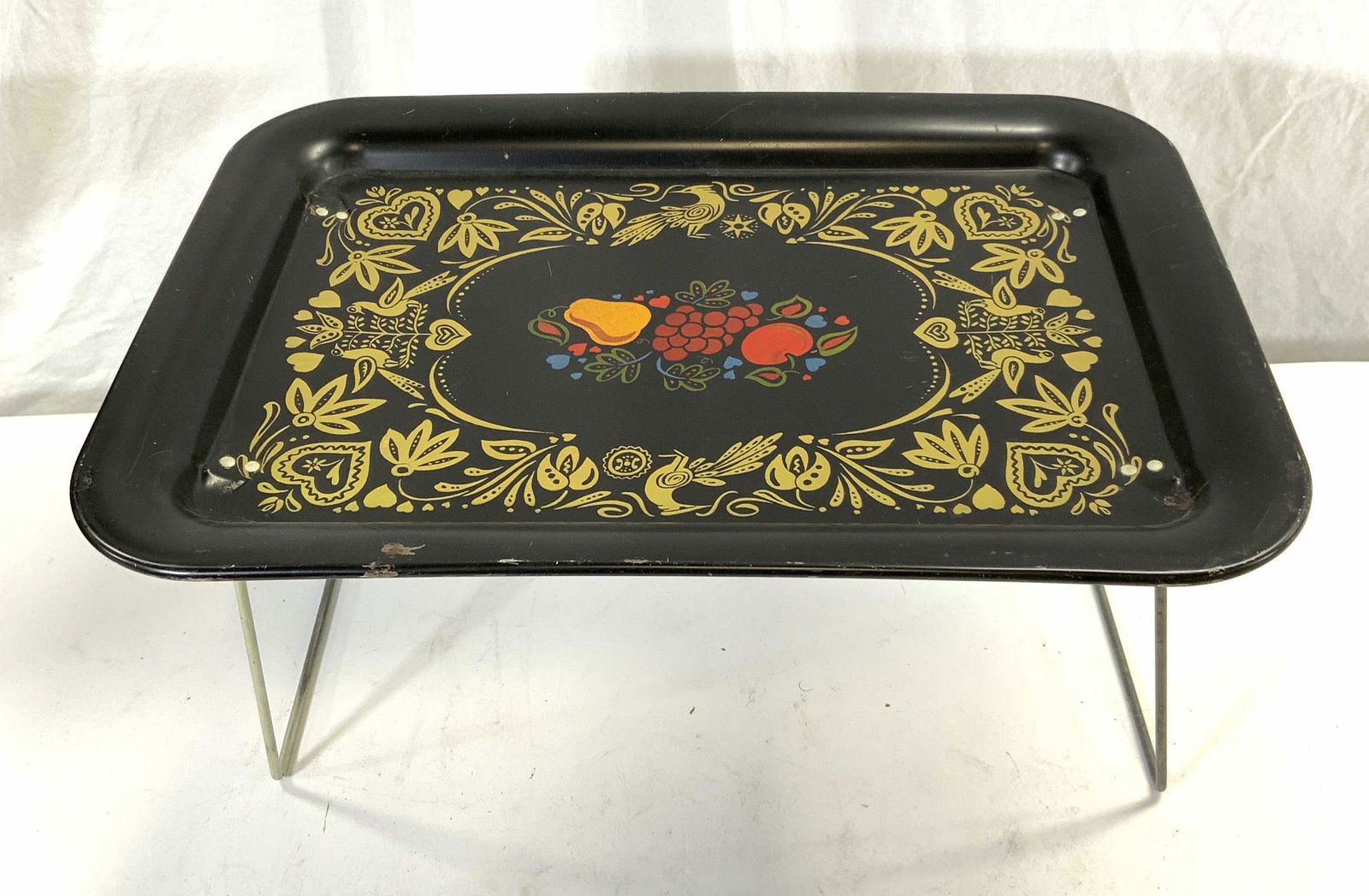 Enameled Metal Fruit Motif Folding Tray: Enameled Metal folding tray with fruit and botanical motif. Measures approx. 17.5 x 12.75 x 8.5 inches. Surface wear consistent with exposure. Folding tray, table tray, table top tray, table accessori