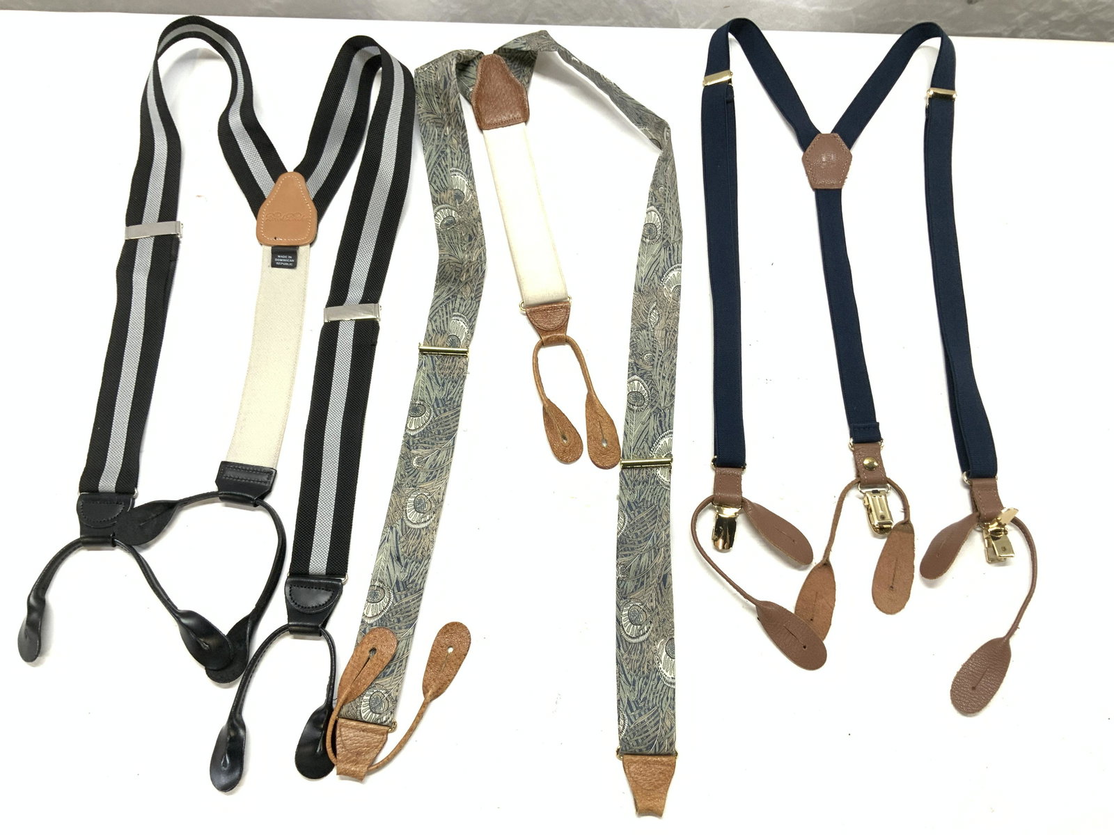 Lot 3 Mens Suspenders, Brooks Brothers: Mens suspenders accented with genuine leather parts. One name brand is Brooks Brothers, another is marked JJ. Stretch suspenders in navy blue and black with grey stripes, one with a floral cotton fabr