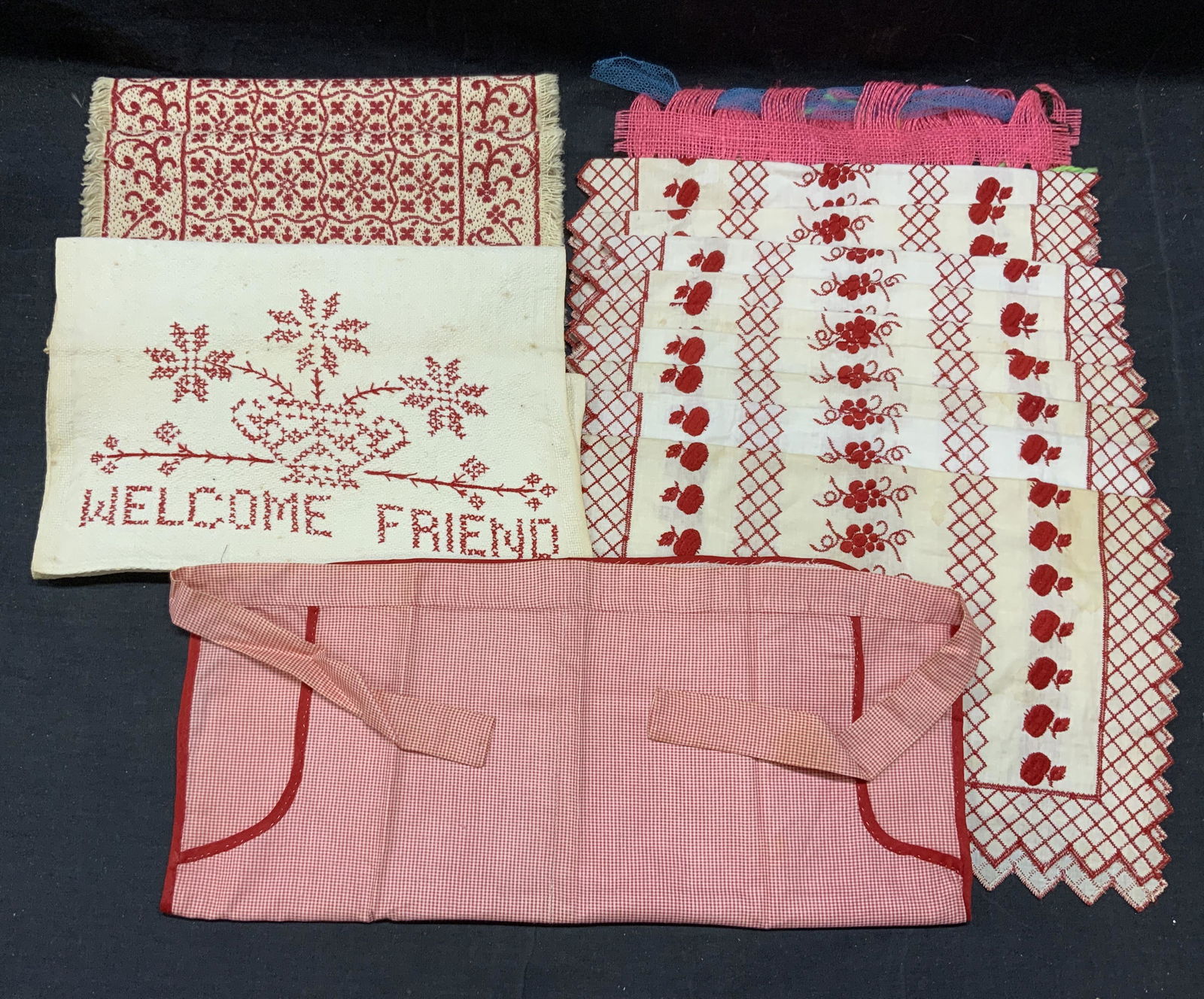 14 Table Linens, Placemats, Apron, More: Lot of 14 table linens & waist apron. Red gingham waist apron, measures approx. 35 inches total waist length. Material feels like cotton, some blemishes observed. Hand embroidered tea towel, reads Wel