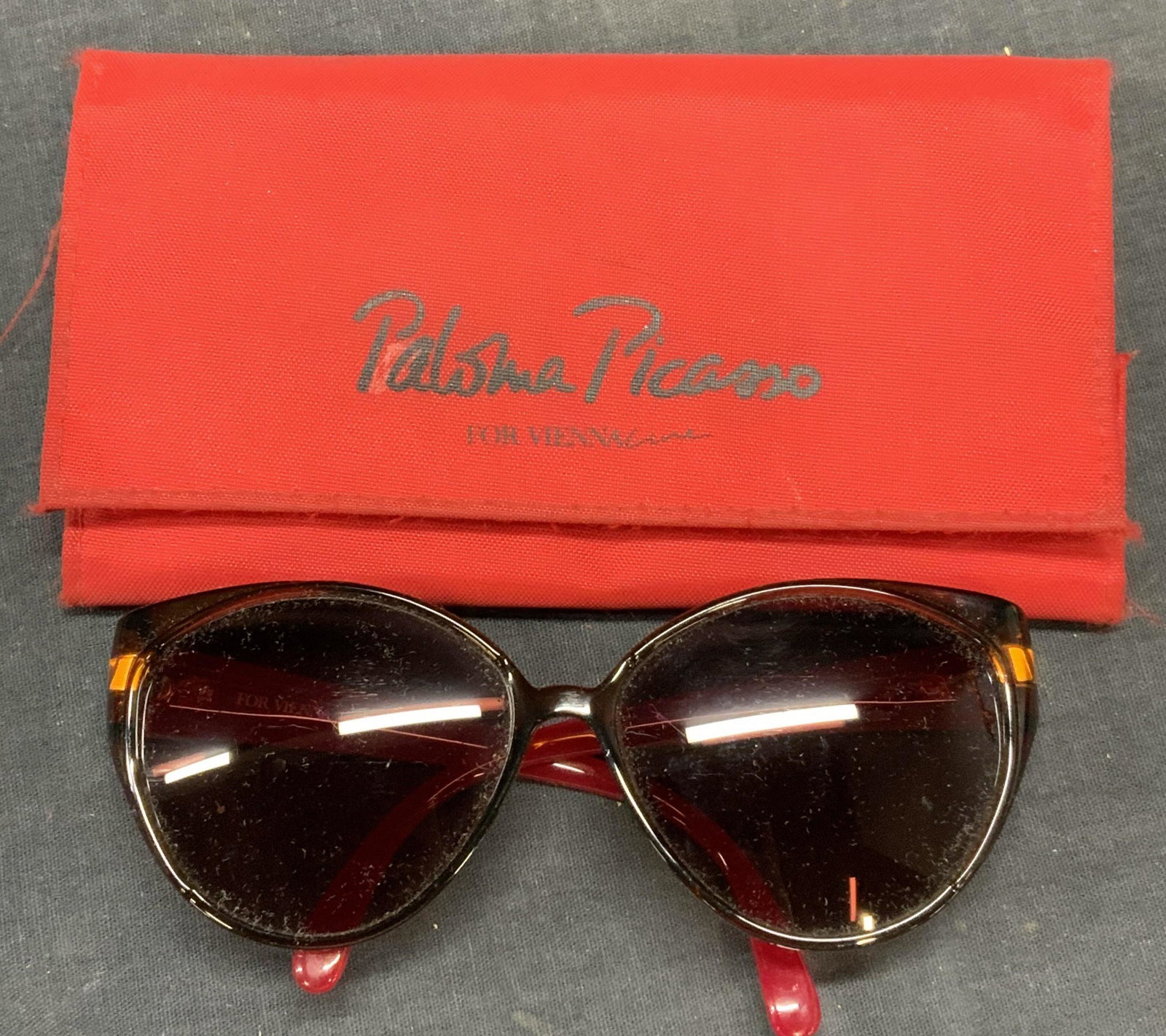 Paloma Picasso Brown/Red Frame Sunglasses: Paloma Picasso brown and red acrylic frame sunglasses and case. Designer label on arm. Measure approx. 5 x 5.5 x 2 1/8 inches. Some surface wear consistent with exposure. Paloma Picasso, Paloma Picass