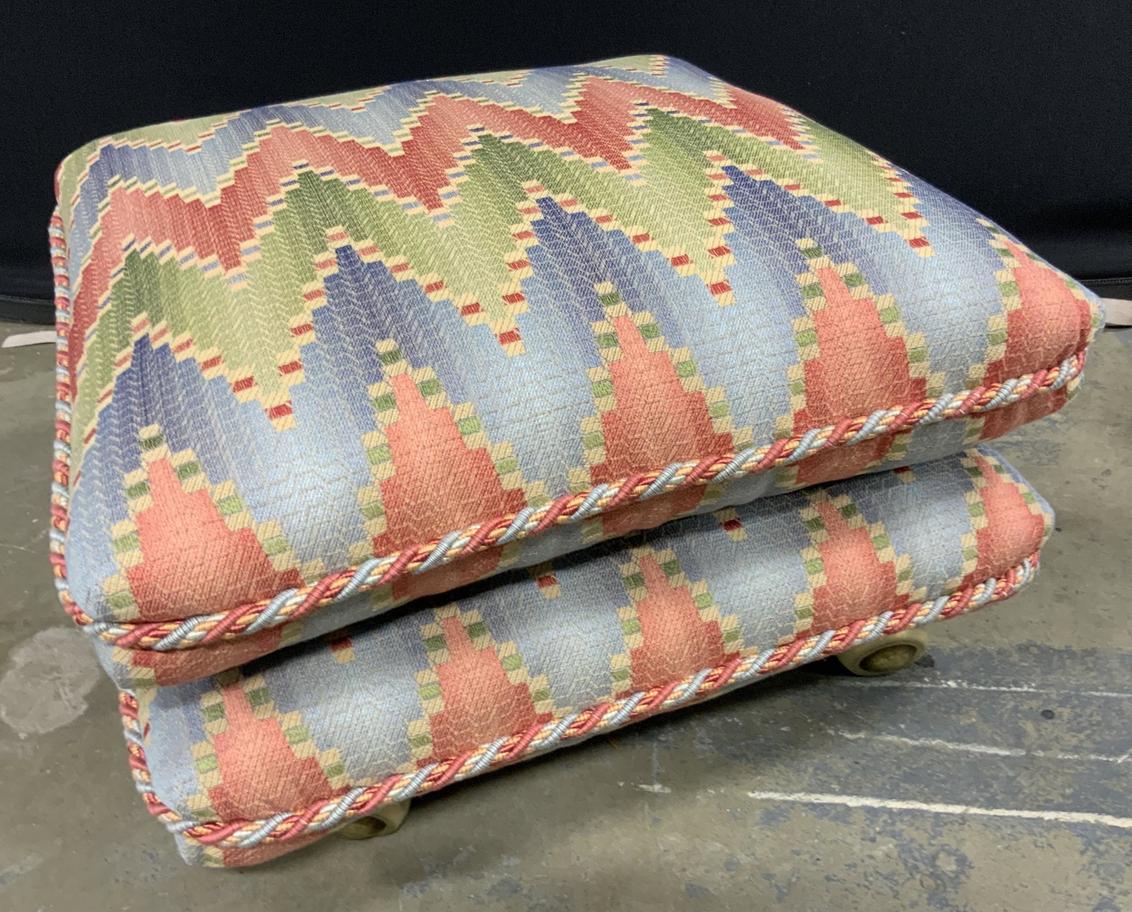 Vintage Geometric Upholstery Wheeled Ottoman: A vintage wheeled ottoman with geometric patterned upholstery. Braided edges. Cushion is removable. Four wheels to underside. Soft hand upholstery, no material tag. Measures approx 12H x 23.5W x 23.5D