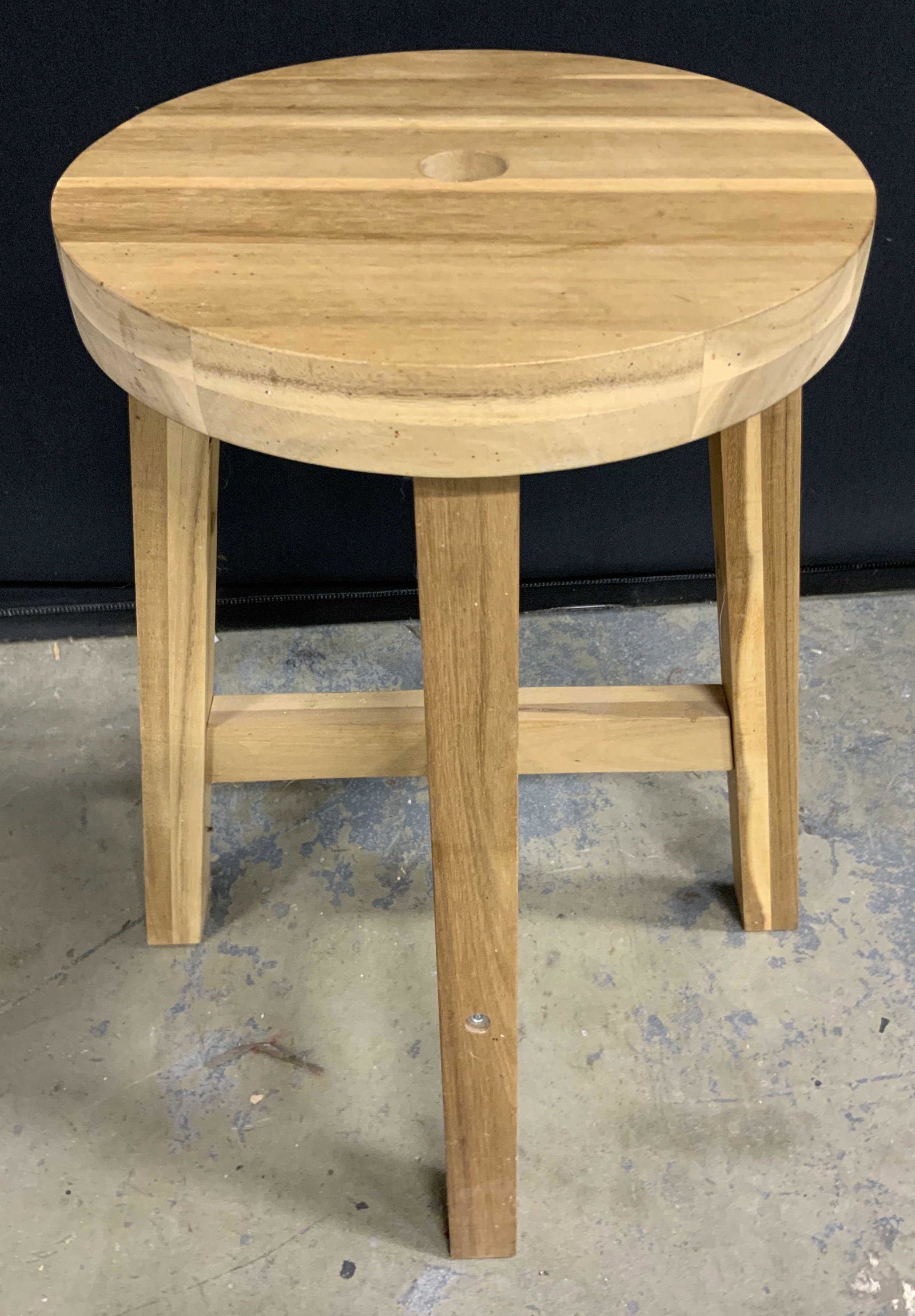 Circular Wooden Stool: A circular wooden stool. Crafted from light hued wood. Drilled hole to the center. Four legs with X shaped stretcher. Some wear consistent with use. Measures approx 18H. Seat measures approx 11W x 11D
