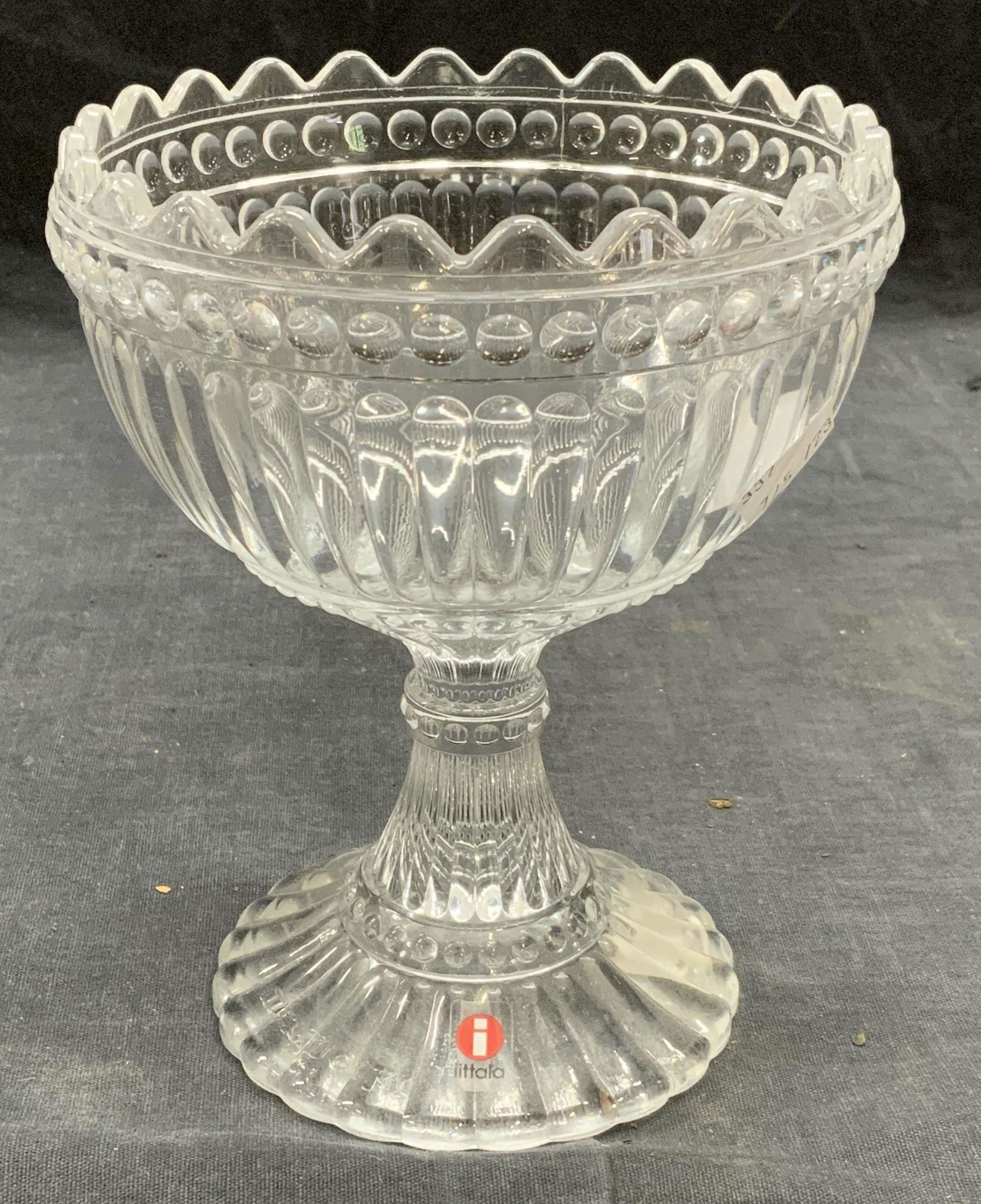Marimekko Iittala Footed Glass Bowl: Marimekko Iittala footed glass bowl with ribbed, bead, and scalloped pattern. Trademarked to underside. Measures approx. 4.75 inches diameter and 6 inches tall. Some surface wear consistent with expos