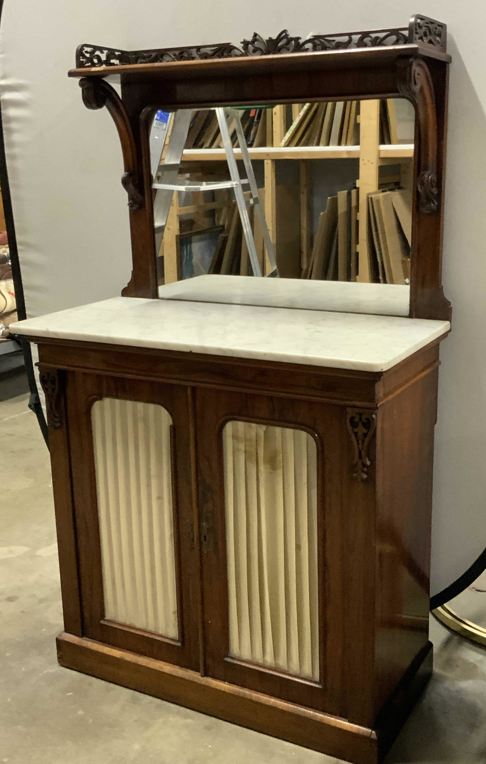 Antique English Wood & Marble Mirrored Chiffonier: An antique English chiffonier with a removable marble top. The marble top is comprised of gray and white hues. Crafted from a rich brown hued wood that features carved scrollwork and open woodwork. To