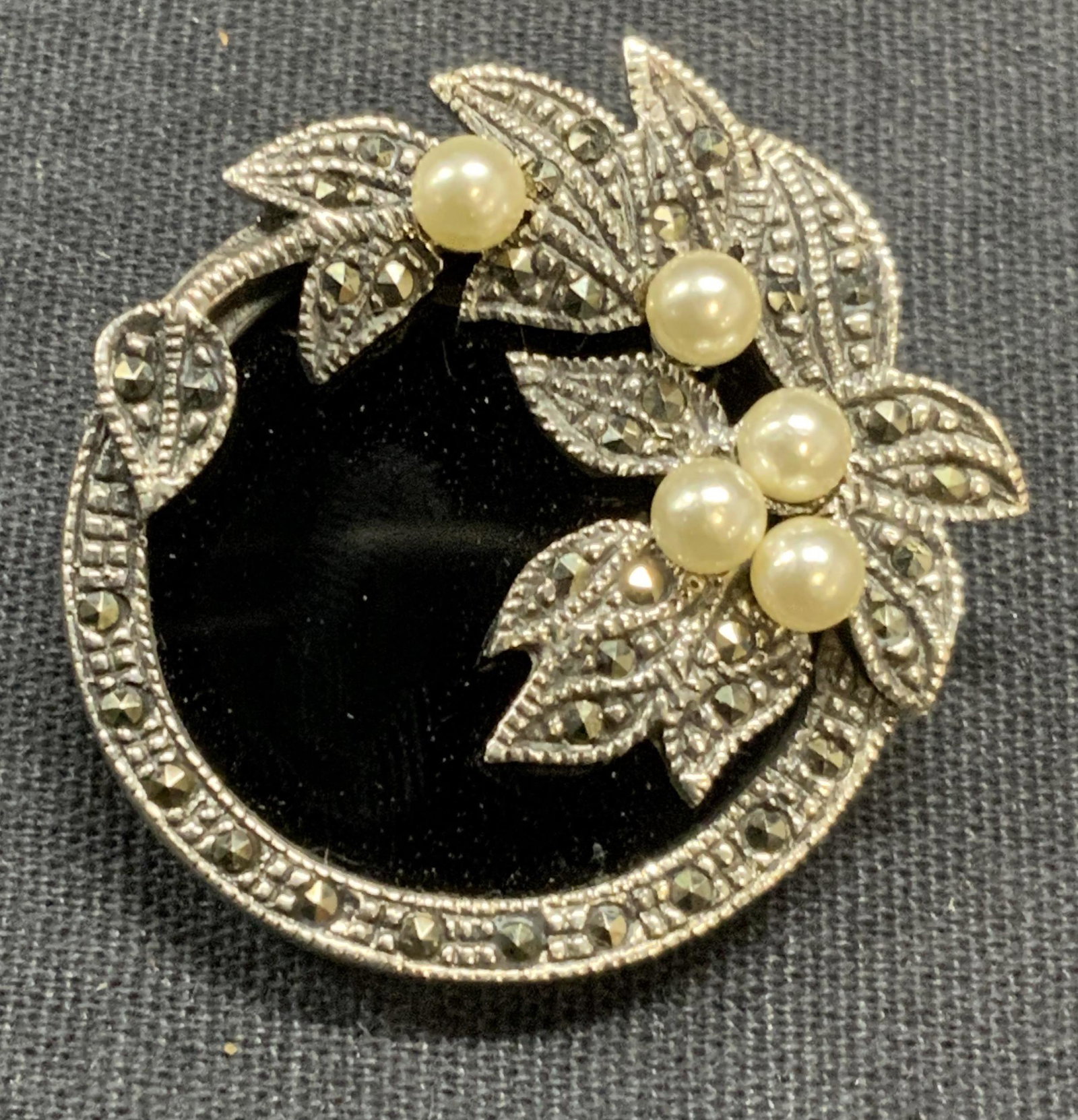 Sterling Silver, Marcasite & Faux Pearl Brooch: Sterling silver brooch with marcasite, faux pearl and black Cabochon decoration. Floral motif. Hinge pin to underside. Measures approx. 1.25 inches wide. Some surface wear consistent with exposure. To