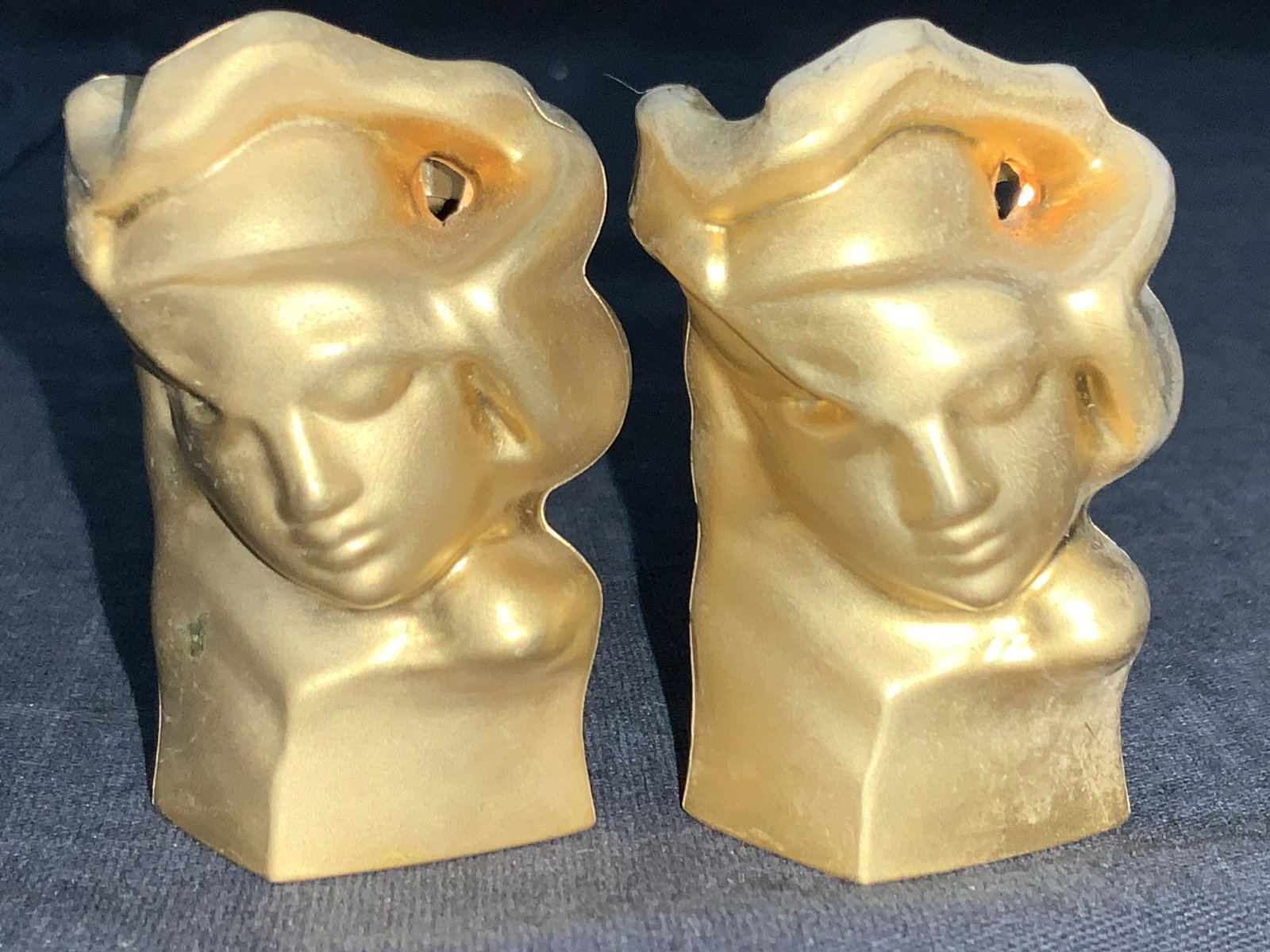 2 Gold Toned Perfume Bottle Topper Heads: Pair of gold toned metal perfume bottle topper heads from perfume Eau du Soie couple d’ornano. Depicts abstract sculptural elements with a face within it. Approximately 2 inches tall. Moderate weari