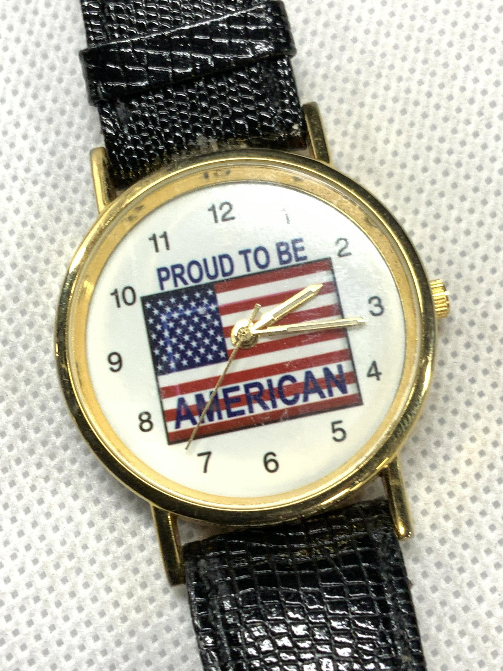 Proud To Be American Leather Wrist Watch: Leather strap wrist watch with clock face that reads Proud to be American with an American flag in the center. Straps are marked Genuine leather, stingless steel back. Approximately 9 inches long and 