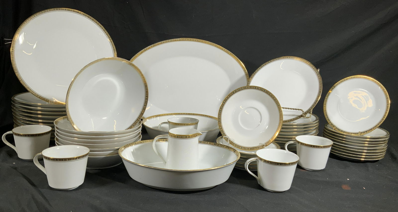 NORITAKE GOLDLANE Lot 54 Porcelain Serveware Set: Undersides each read NORITAKE GOLDLANE. Each piece has gilt rims. Lot includes 11 dinner plates, 10 salad plates, 10 bread plates, 8 bowls, 6 saucers, 1 oval serving dish, 1 serving bowl, 1 oval servi