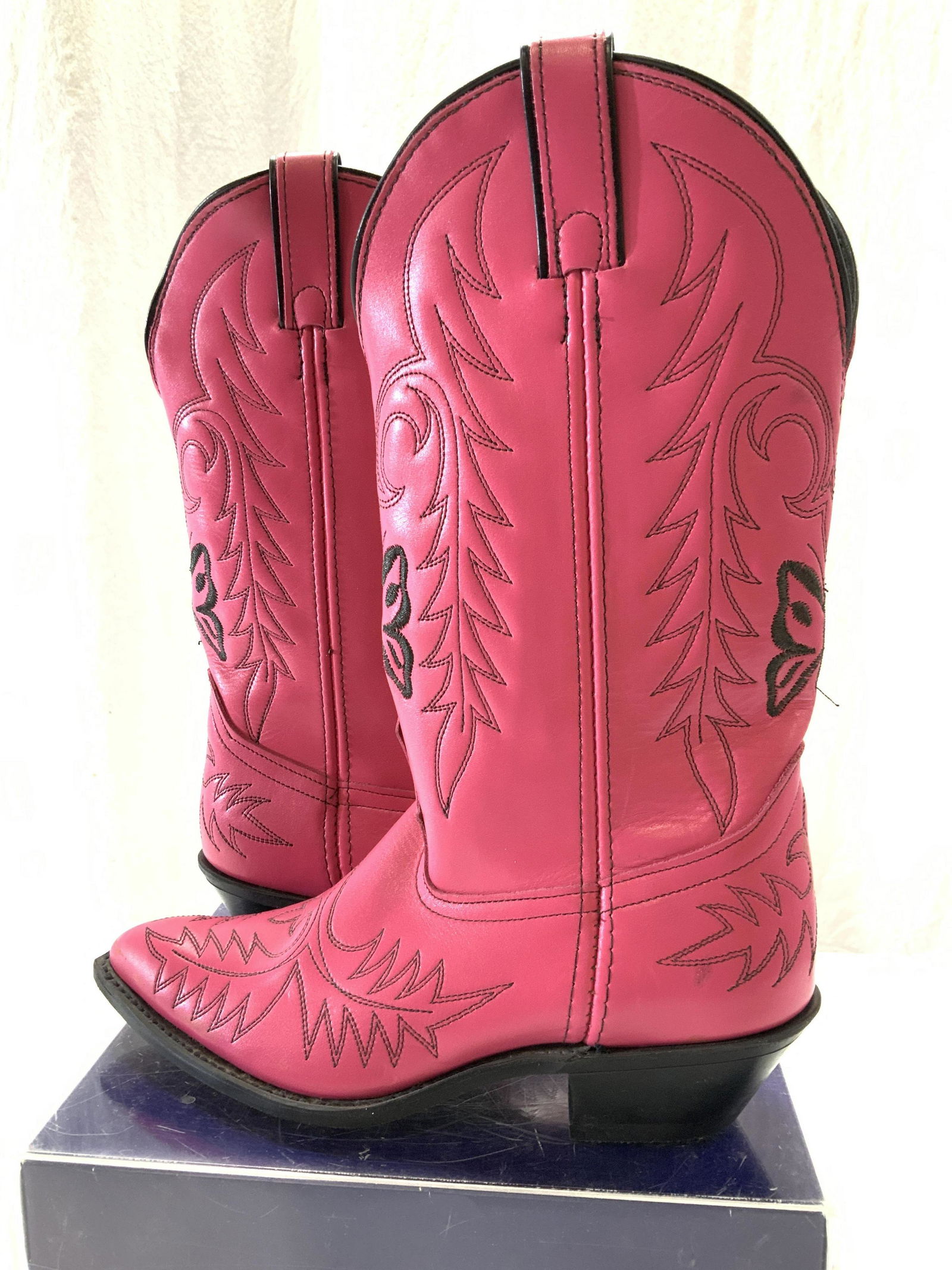 Embroidered Pink Leather Cowgirl Boots: Slip on cowgirl boots, bright pink with black stitching , butterflies and western fauna pattern. Pointed toe box, unmarked brand, possibly leather or man made leather. 2 in. heel. Widest part of toe b