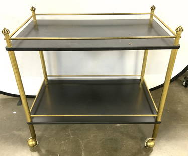 Vintage Two Tier Gilt Metal Tea Cart: Tea cart is vintage. Piece has 2 black toned tiers. Frame appears to be gold toned gilt metal or brass. Measures approximately 31 inches long 30 inches tall 18 inches deep. Top of piece has gold toned