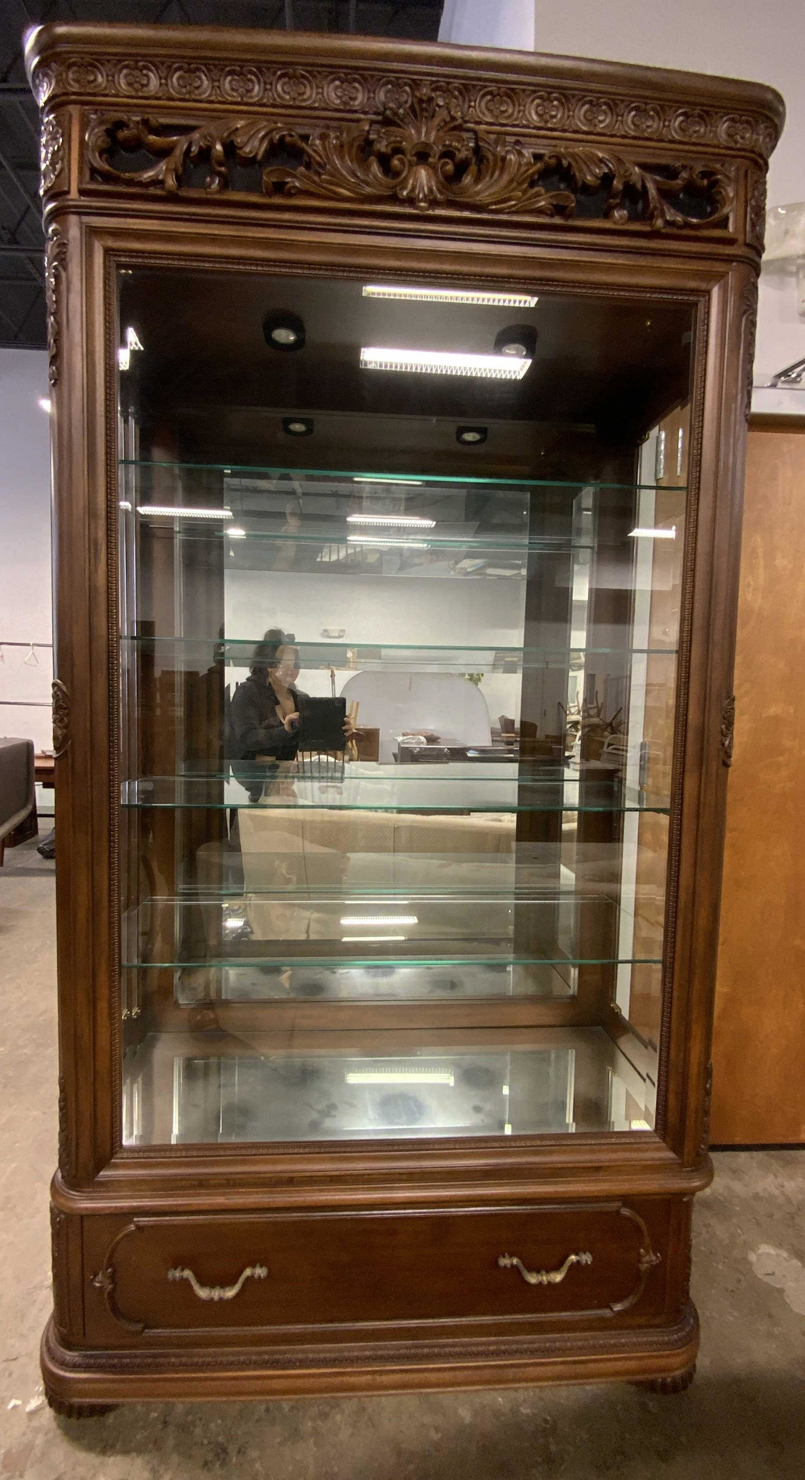 JESSICA MCLINTOCK HOME Romance Collection Cabinet: A carved wooden display cabinet with glass shelving and a mirrored back. Both sides open in order to access interior. Brass hued metal drawer and door pulls. One drawer to obverse. Plaque to interior 