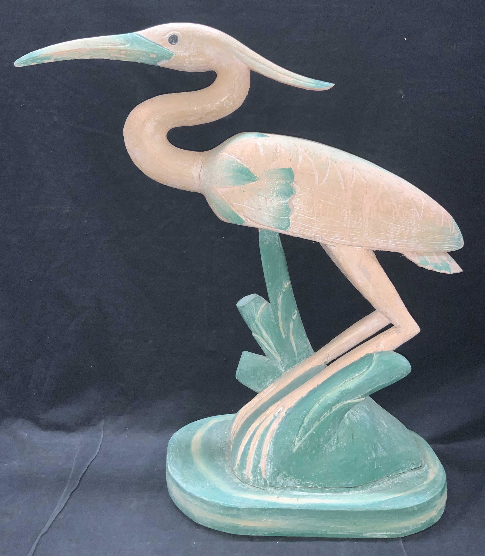 25 Inch Tall Hand Carved Crane Folk Art Sculpture: Hand carved and painted wooden sculpture of a crane, possibly an egret. Painted pink and resting on a teal toned base with teal toned accents. Approximately 25 inches tall and 28 inches wide. Evident 