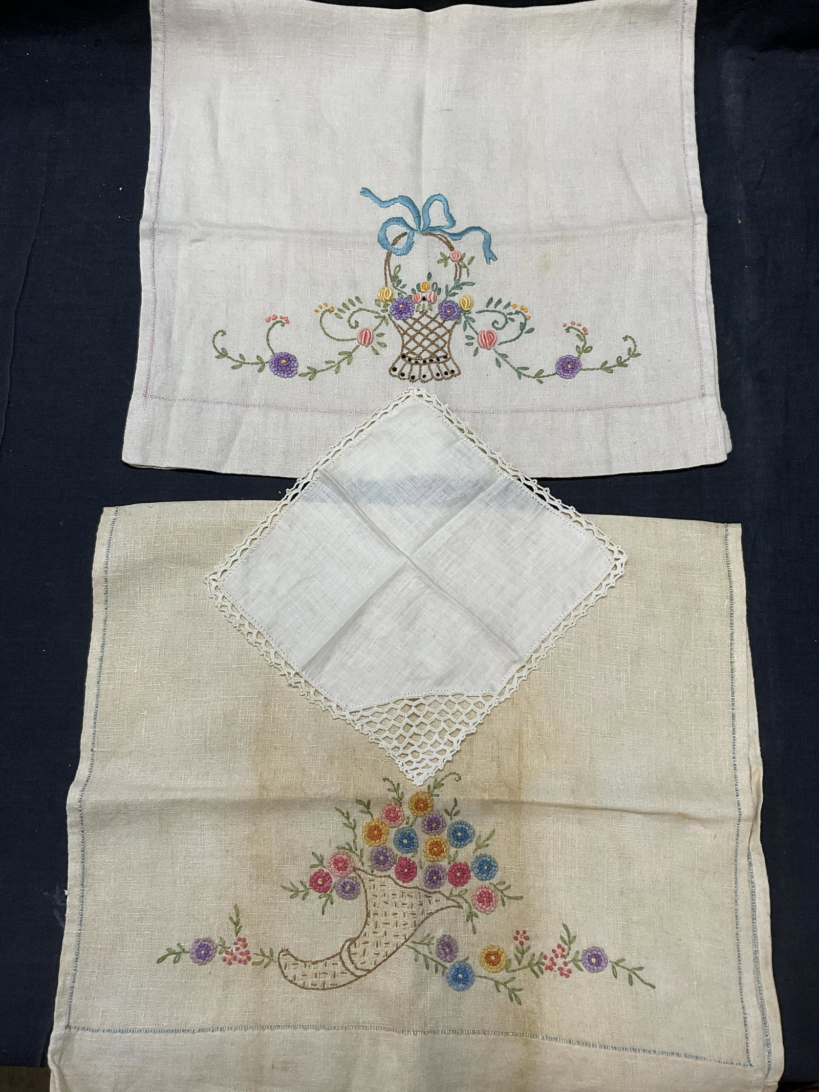 Lot 3 Tabletop Embroidered Linens: Embroidered floral tabletop linens. 2 embroidered cloths, 1 small doily. Significant staining and discoloration to fabric (see photos). Largest pieces measures approx 15.25 x 27.75 inches. No material