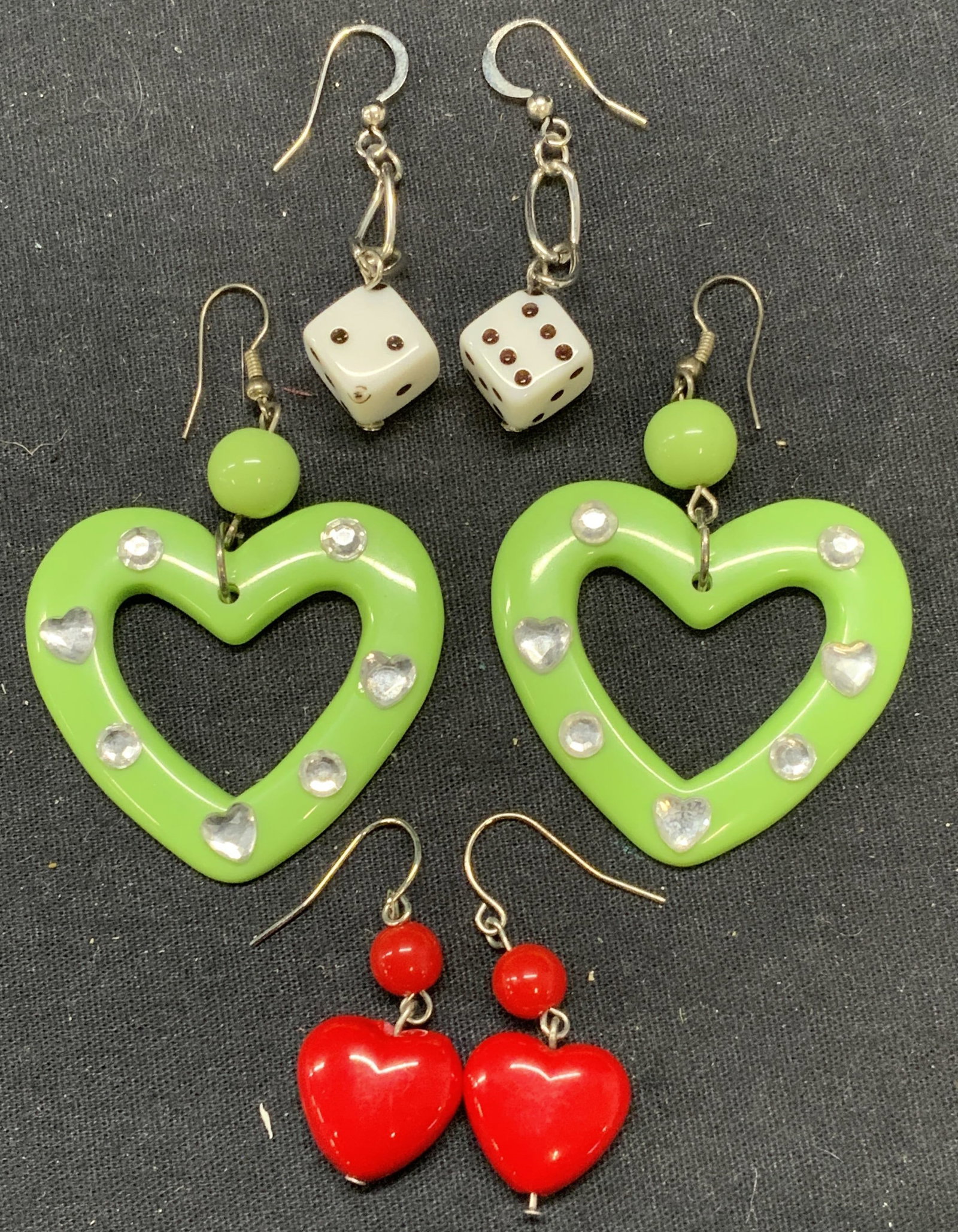 Lot 3 Heart & Dice Dangle Earrings: Lot of 3 jewelry pieces. Green acrylic and crystal heart dangle earrings. Measure approx. 2 x 1.75 inches. Red acrylic heart dangle earrings. Measure approx. 1.25 x 5/8 inches. White acrylic dice dang