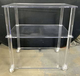 MCM Lucite Bar Cart On Wheels: Bar cart is mid century modern. Piece has top center & lower tier. Cart sits on 4 spherical shaped wheels. Piece has cylindrical shaped supports. Cart measures approx 27 inches long 24 inches tall 16