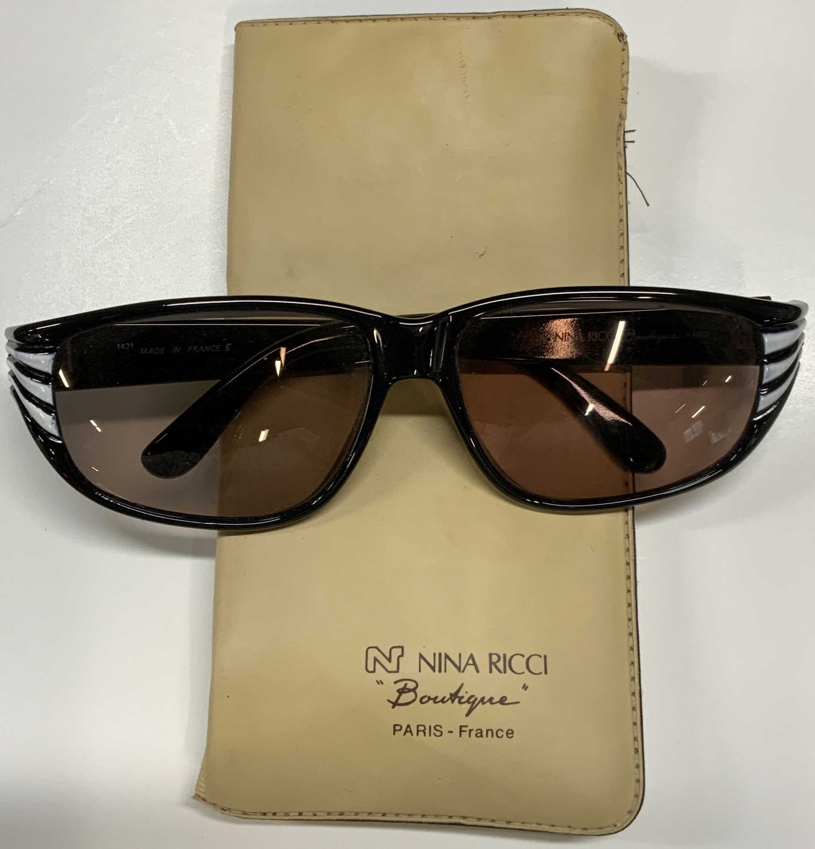 Nina RICCI Boutique Black Sunglasses, France: Nina RICCI Boutique black and white acrylic frame sunglasses and Nina RICCI case. Designer label on arm. Made in France. Surface wear consistent with exposure. Measures approx. 5 x 5.5 x 1.75 inches. 