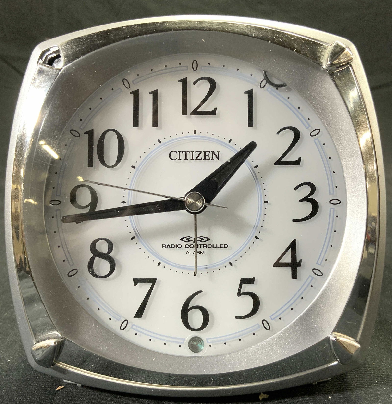 CITIZEN Radio Controlled Alarm Clock: Clock face reads CITIZEN RADIO CONTROLLED ALARM. Piece has silver toned exterior with white toned face, black toned numbers. Appears to be plastic. Measures approx 4.25 inches tall 4.5 inches wide 3 i