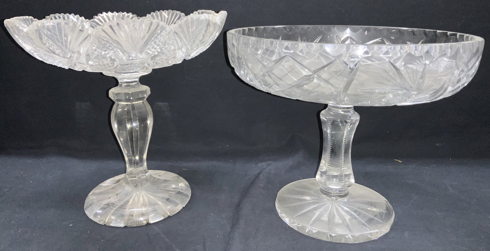 2 Thick Cut Glass Footed Dishes: Set of thick cut glass footed bowls. 1 with saw tooth edges, at 9 inches tall and 9 inch diameter and the other with thick cut bowl with Star burst cuts on exterior at 8.5 inches tall and 10 inch diam