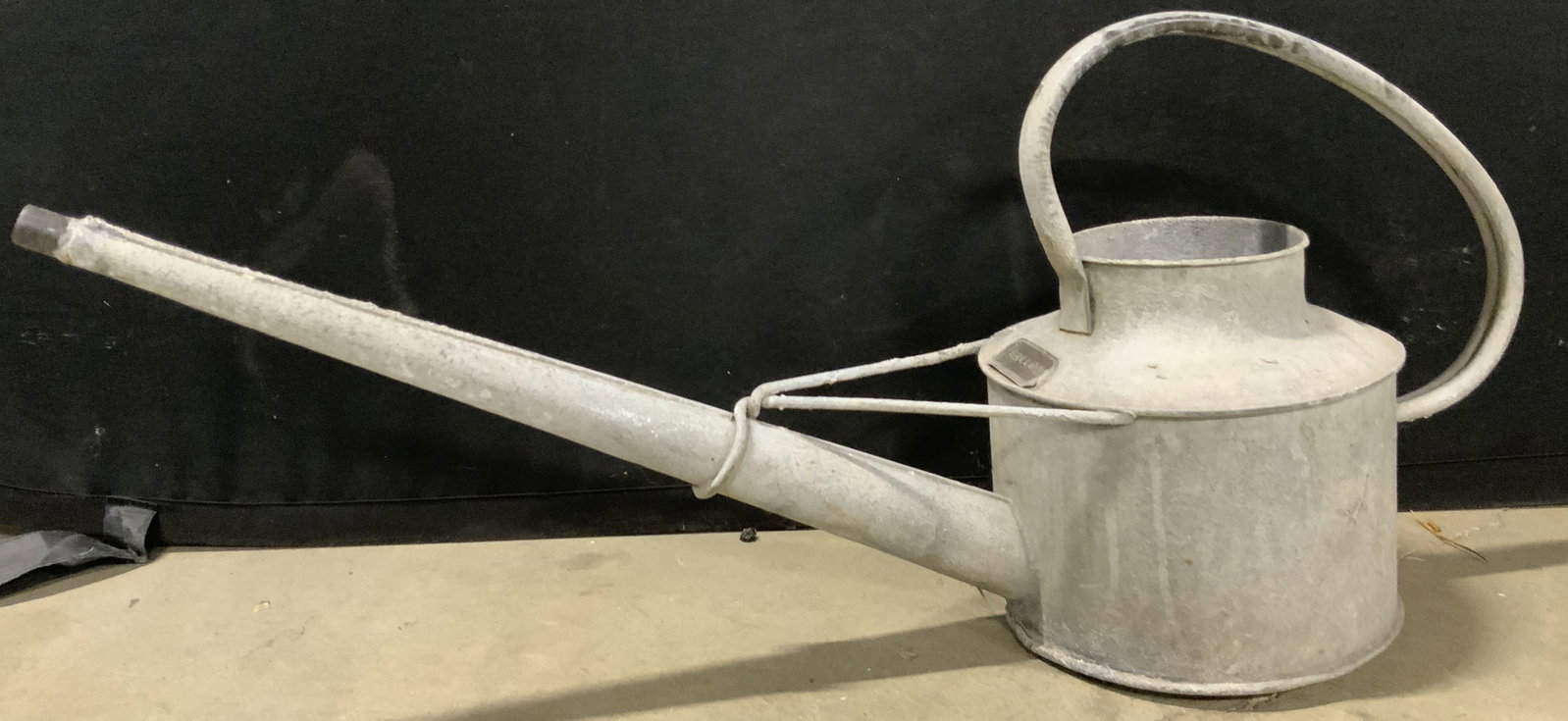 Vintage Metal Watering Can: A vintage metal watering can. Gray hued metal. Obverse features a metal plaque which in numbered 34 and reads GALLON. Measures approx. 11.5H x 26W in. Some surface wear consistent with age, use, and e