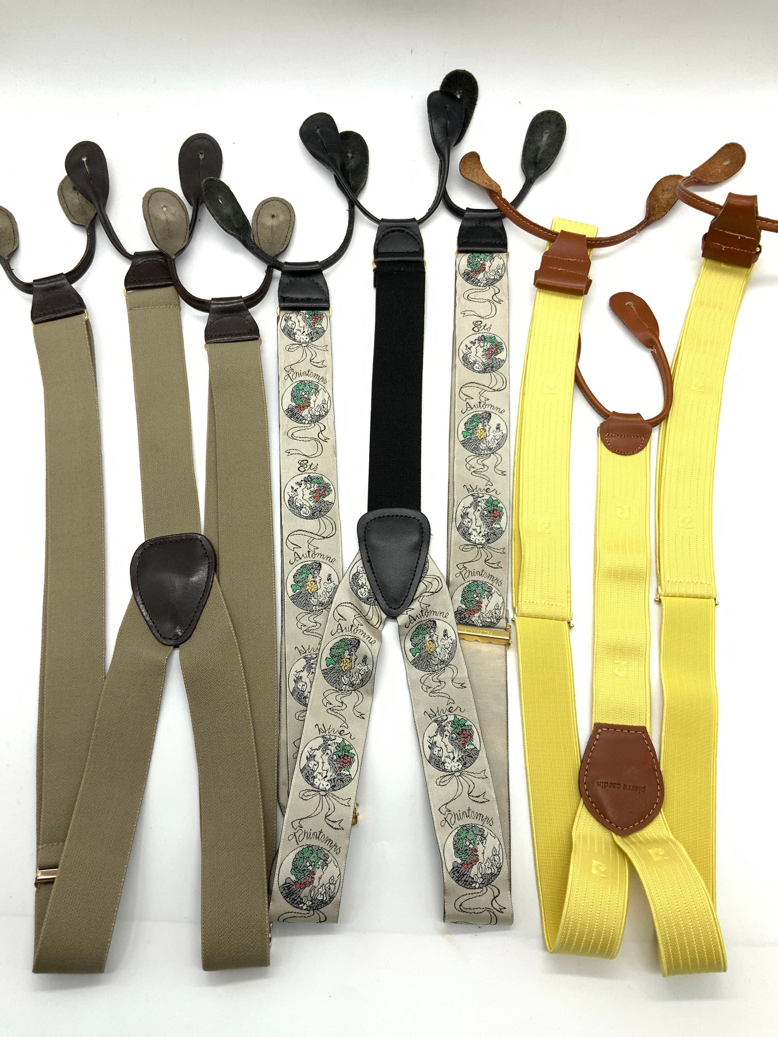 3 Assorted Suspenders, Pierre Cardin & More: Group lot of 3 Assorted suspenders. 1 marked Pierre Cardin with yellow bands, 1 with off gray bands and 1 with various profiles of women. All with colored leather ends. Approximately 30 inches long. M