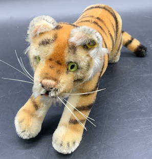 STEIFF Vintage Stuffed Toy Tiger Plush: A vintage stuffed tiger plush. Orange and black hues. Light green composite eyes. Clear plastic wire whiskers. Metal to ear reads STEIFF. Measures approx. 5H x 10W in. Piece has some wear consistent w