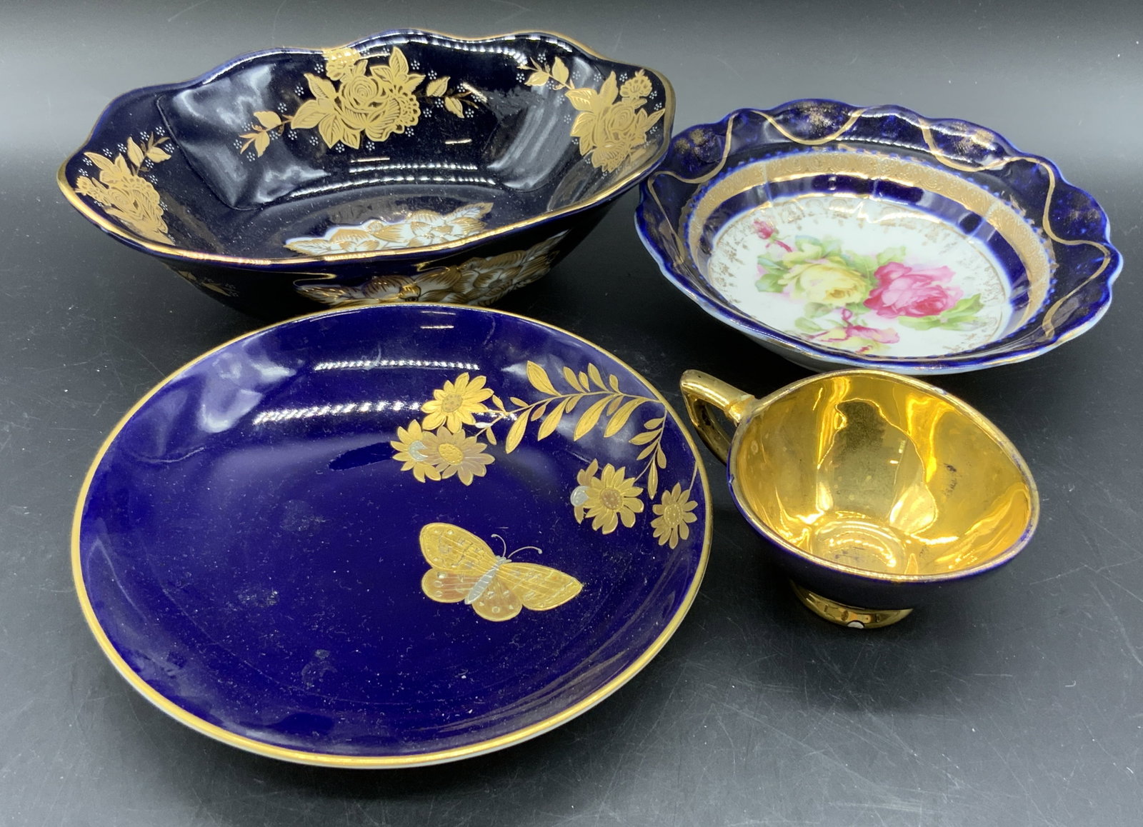 Lot 4 Blue & Gilt Porcelain Teacup & Plates: A lot of four deep blue and gilt porcelain teacup and plates. Primarily floral and crest motifs throughout the pieces. Brands include MINTONS, KHM, I HUN MZ, and IPF Germany. Repairs present, some los