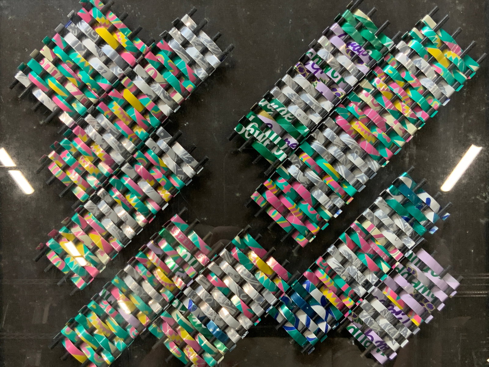 JAMES MOSIER & Co Signed Ice Tea Can Woven Art: Signed on lower right corner James MOSIER and Woody Sarad. 1995 Depicts various woven panels made of Arizona ice tea cans affixed to a black background Framed in black toned metal frame with green blu