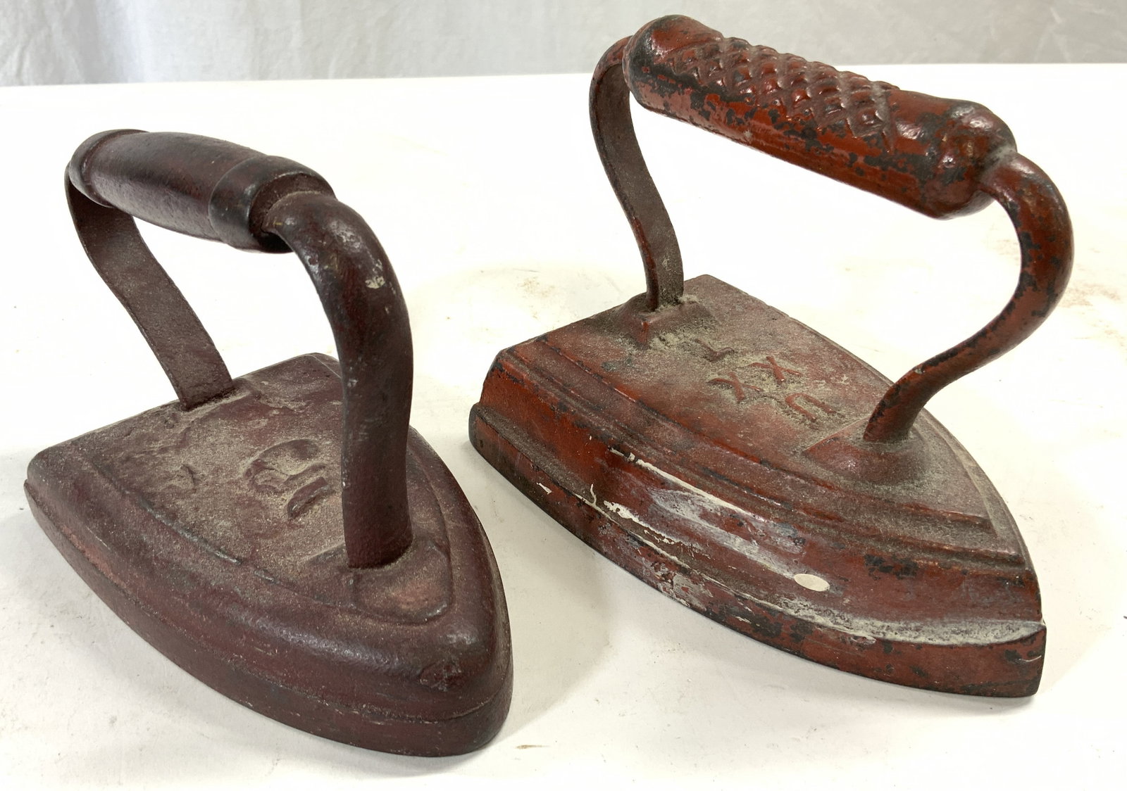 Lot 2 Antique Irons Red: Lot includes 2 Irons. Each are red toned. One has number 5 on top the other reads U XX T. Each piece is significantly weighted. Larger iron measures approximately 6 inches deep 5 inches tall 3.5 inche