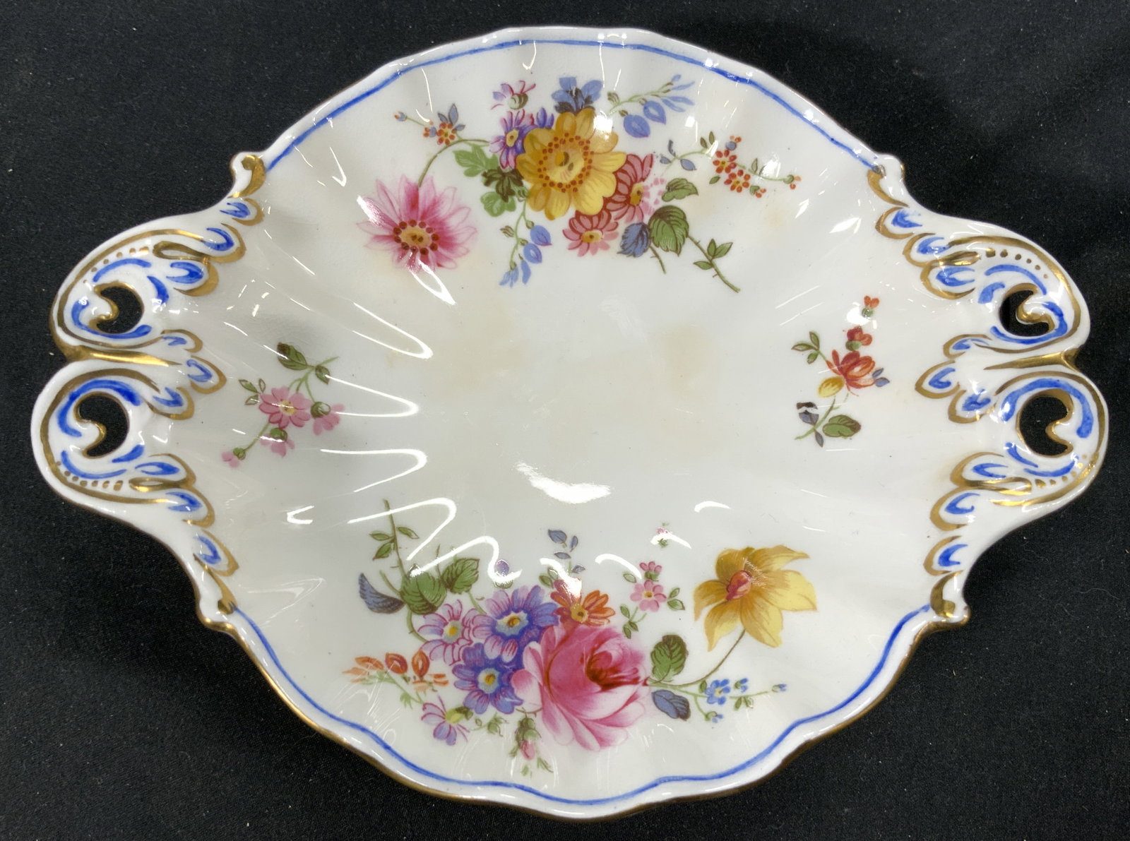 ROYAL CROWN DERBY Porc Scalloped Footed Bowl: Underside is marked ROYAL CROWN DERBY. Piece is vintage & porcelain. Vessel is white with multi toned floral & leaf detail. Piece has pierced detail in handles. Vessel has scalloped sides & gilt detai