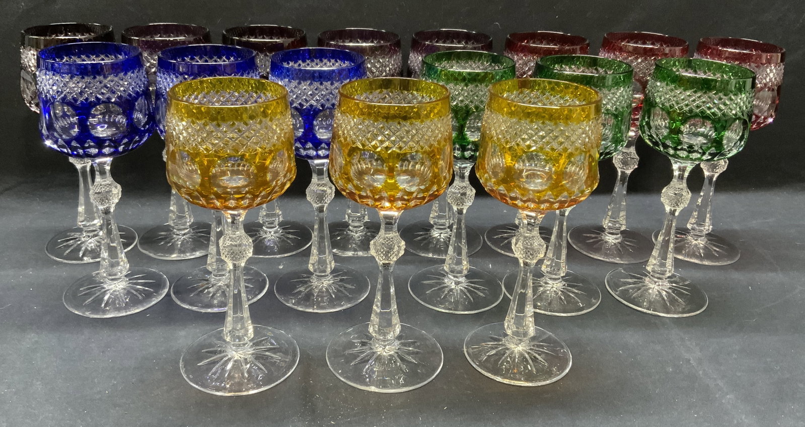 Set 17 Colored Cut Crystal Wine Glasses: Set of 17 cut crystal wine glasses. Yellow, purple, red, blue, and green to clear. All pieces have some surface wear consistent with exposure including small chips observed. Measure approx. 3.25 x 7.7