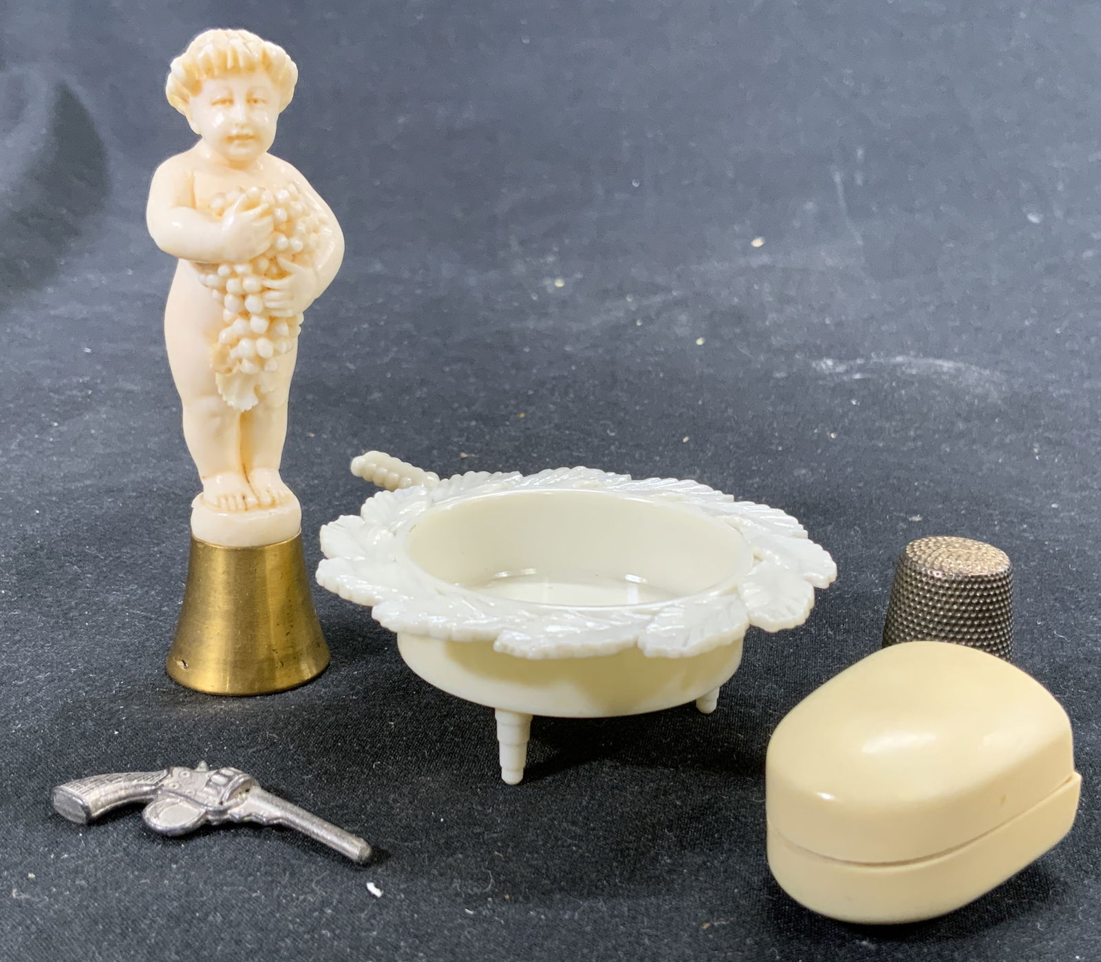 Lot 5 800 Silver Thimble & Other Tabletop Accs: Thimble figure reads 800. Lot includes 1 thimble figure weight .11 OZT, 1 metal pistol figure, 1 cherub holding grapes figure on brass base possibly bone, possibly Bakelite, possibly a resinous materi
