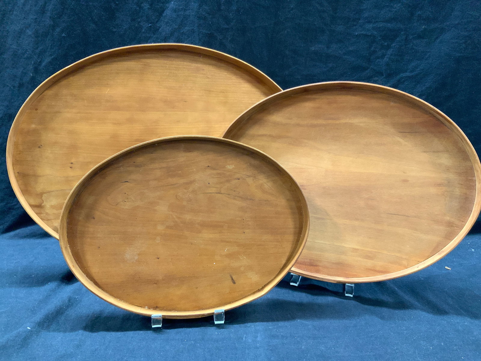 3 Canterbury Woodworks Wooden Table Trays: 3 wooden table trays, marked on undersides Canterbury Woodworks, Canterbury, NII. Three different size trays in tan toned wood, largest being 20 inch diameter and smallest is approximately 13 inch dia