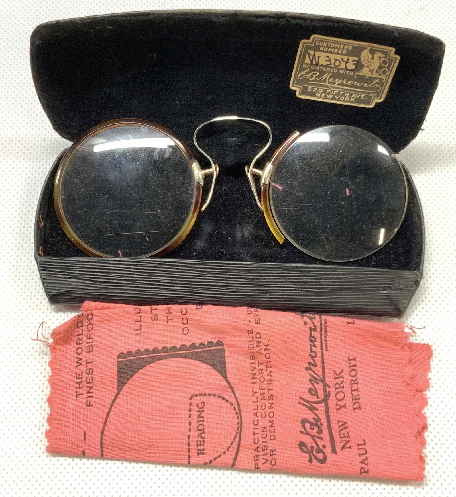 Vintage Univis Bifocal Spectacles W Case: Vintage pair of bifocal glasses with no arms, frame is made of wire and plastic framing around glass. Comes with black case that reads E,B.Meyrowitz, incorporated. New York, Minneapolis, St.Paul, Detr