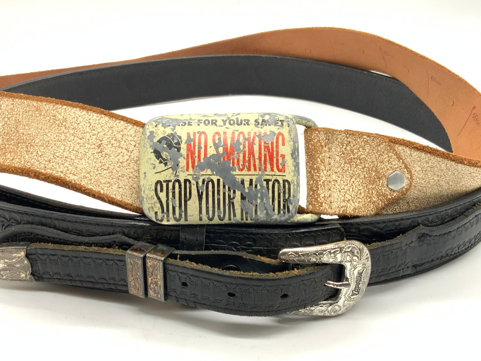2 Vintage Nocona & More Leather Fashion Belts: 2 vintage leather belts. 2 black toned leather belts with floral designs within the band and silver coated brass buckle and accents. Approx 47 inches long marked Nocona on interior of belt. Other is t