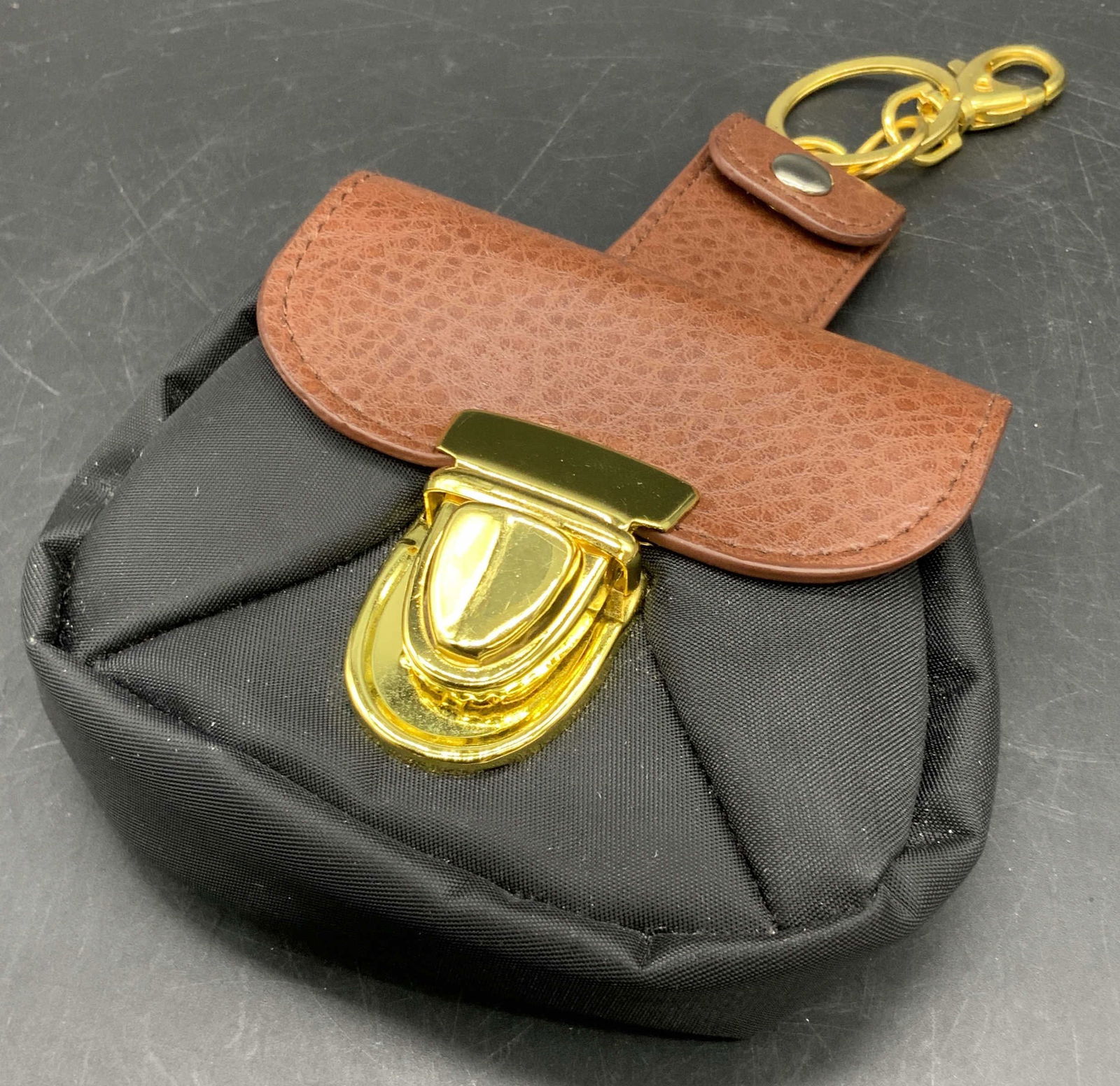 Black & Brown Coin Purse Keychain: A black and brown coin purse keychain with gold tone metal hardware. Crafted from leather style material and black fabric. Flap closure. Lobster claw clasp to the strap. Measures approx. 4W x 7L in. M