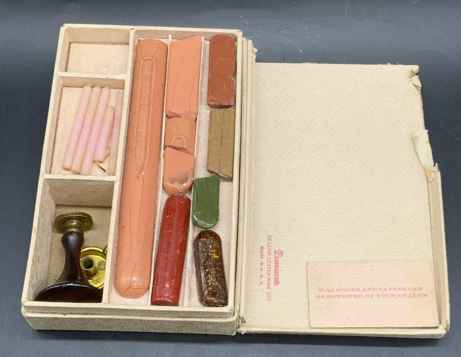 DENNISONS Vintage De Luxe Letter Wax Set, USA: Box reads DENNISONS De Luxe Letter Wax Set Made in USA. Kit comes with wax, a small candle holder, and a wax seal crafted from metal & wood. Contained in a box. Box measures approx. 1.75H x 6.5W in. P