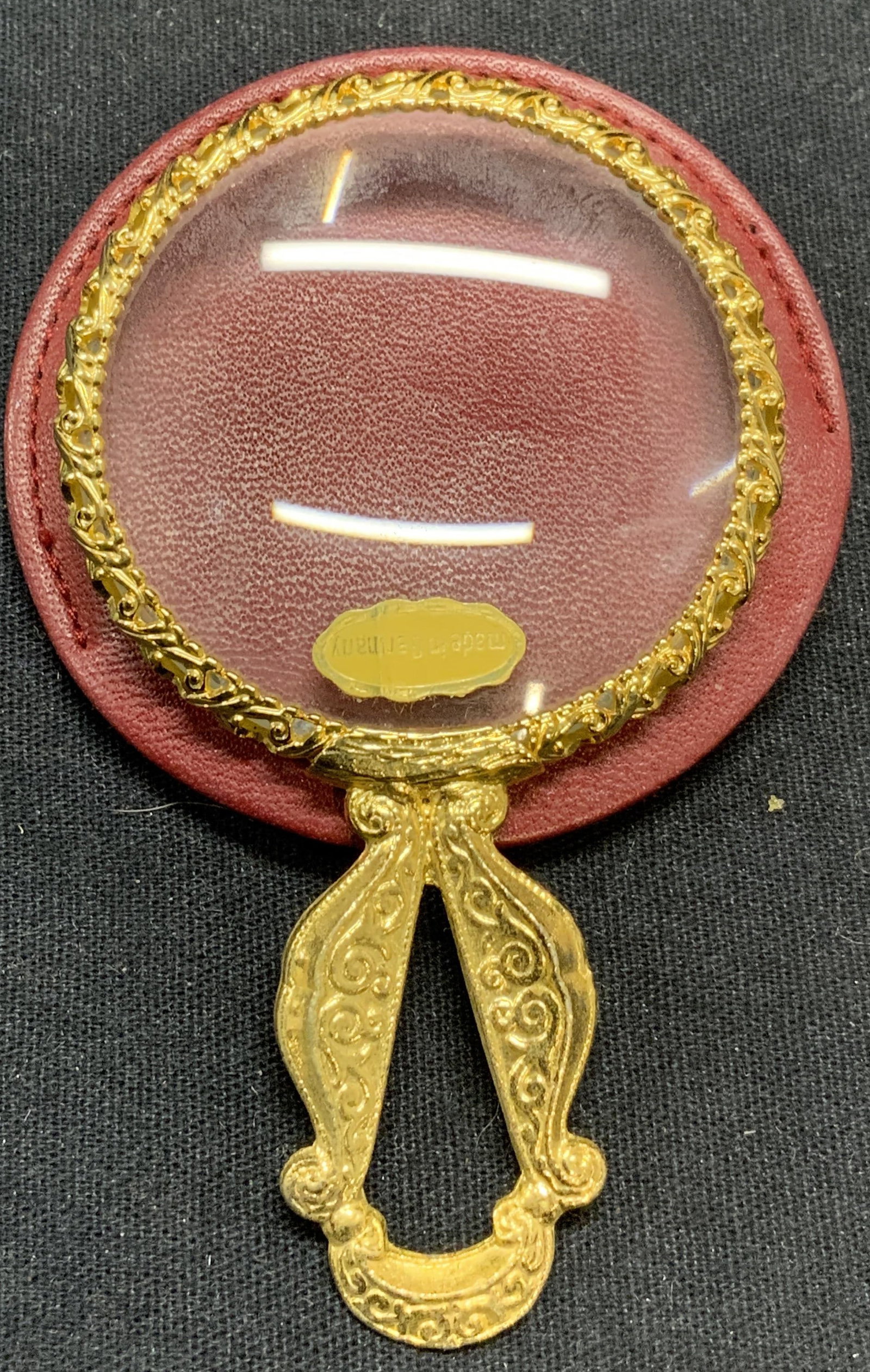Gold Tone Magnifying Glass & Leather Cover: Gold tone magnifying glass with red leather cover. Marked made in Germany. Magnifying glass measures approx. 3 3/8 x 2 inches. Some surface wear consistent with exposure. Magnifying glass, gold tone m