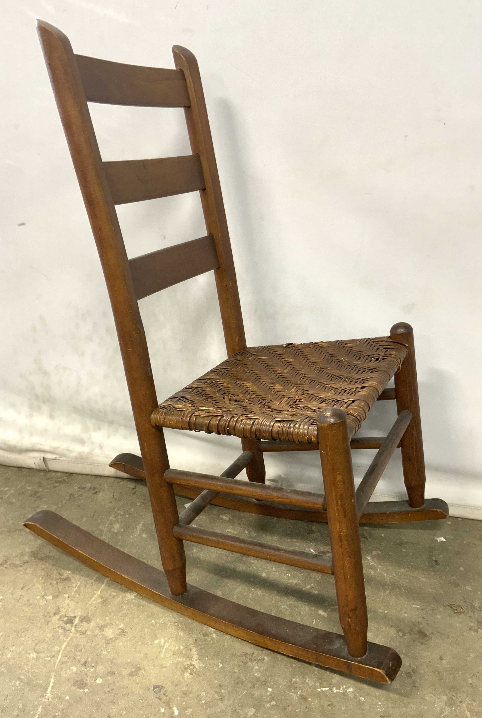 Vintage Wooden Woven Seat Rocking Chair: A vintage wooden rocking chair with a woven seat. Ladder back. Measures approx. 34H x 26.5D x 17W in. Measured at widest point. Depth taken at base. Piece has some surface wear and losses present. Vin