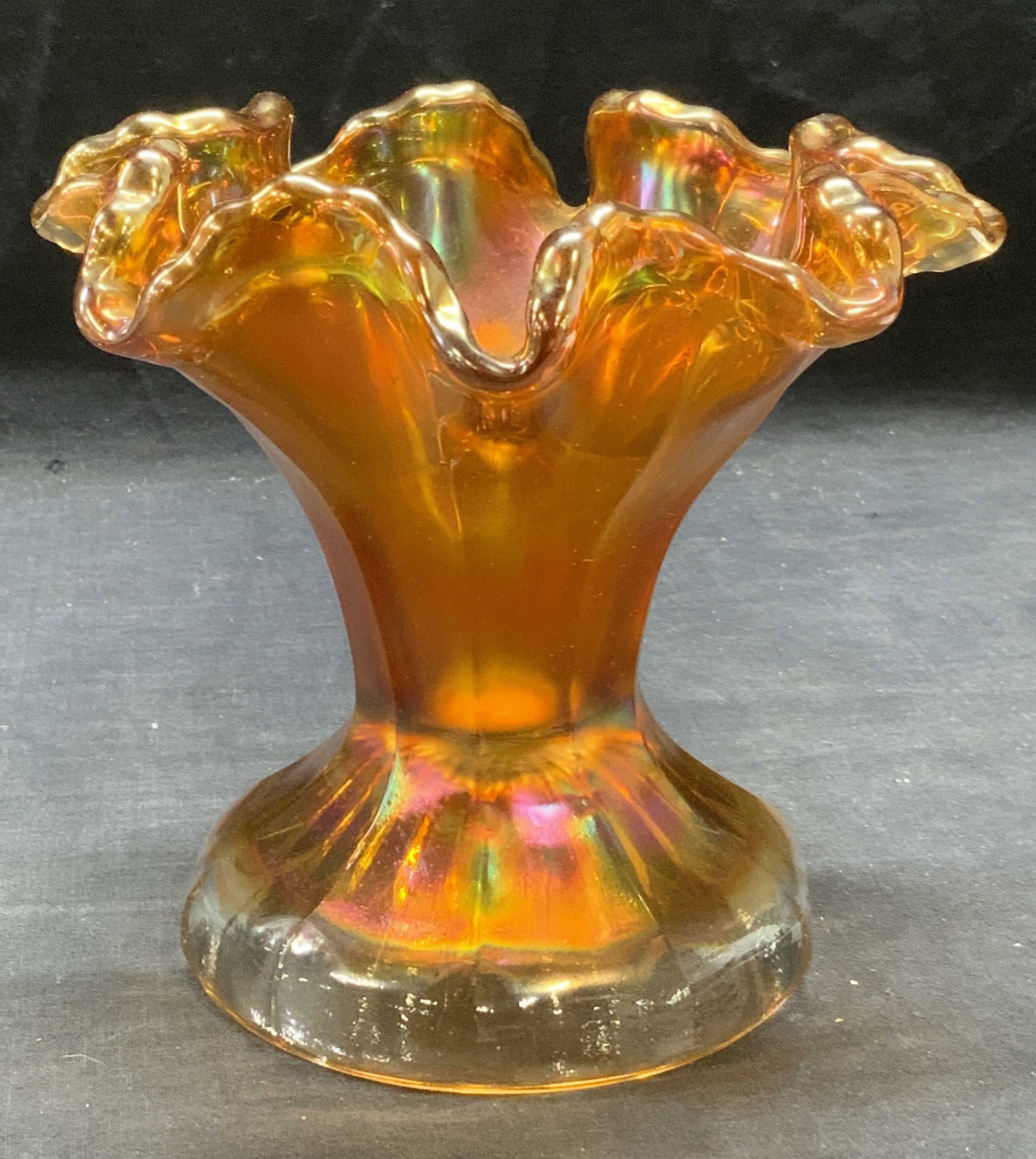 Orange Carnival Art Glass Footed Bowl: Orange iridescent carnival art glass footed bowl with handkerchief rim. Some surface wear consistent with exposure. Measures approx. 6.75 inches wide and 6 inches tall. Art glass, carnival glass, irid