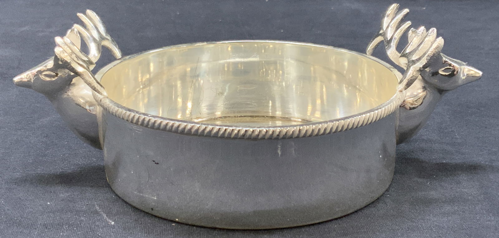 Designco Silver Pate Deer Head Bottle Coaster: Marked on underside Made by Designco, wine coaster. Silver plate over brass coaster either deer or reindeer heads on either side. Approximately 1.5 inches tall and 5 inch diameter. Moderate wearing to