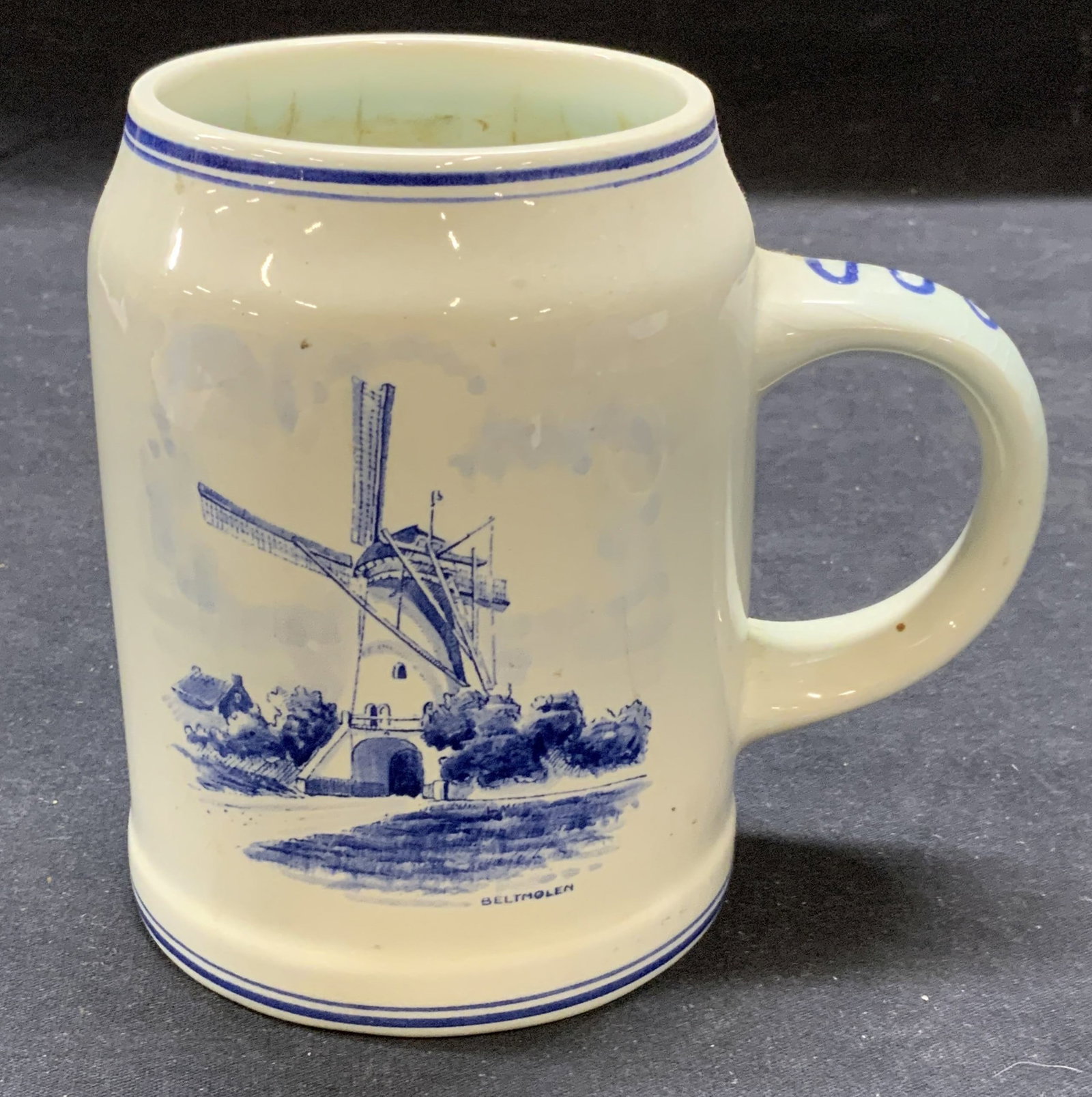 Signed Delft Holland Amsterdam Ceramic Mug: Signed Delft Holland ceramic mug with Amsterdam crest and windmill motif. Signed to underside. Some surface wear consistent with exposure. Measures approx. 4 x 5 inches. Delft Holland, delft Holland m