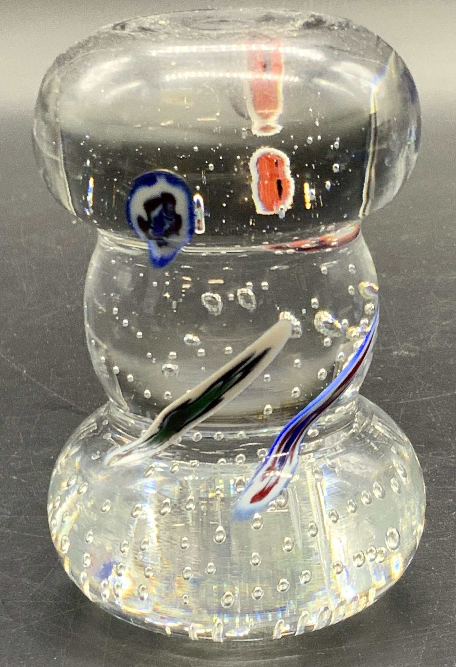 Art Glass Knob Pillar Millefiori Paperweight: A clear art glass knob pillar form paperweight featuring colorful millefiori throughout. Bubbles to interior as well. Measures approx. 4H x 2.25W in. Some surface wear consistent with age and use. Som
