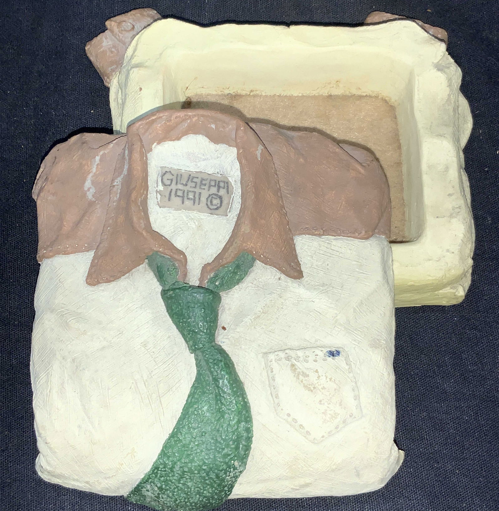 Giuseppi Signed Clay Clothing Trinket Box, 1991: Marked on exterior and interior, giuseppi, 1991. Trinket box that resembles a folded shirt. Approximately 2 inches tall and 4 inches wide. Moderate chipping to edges of clay and wearing due to age and