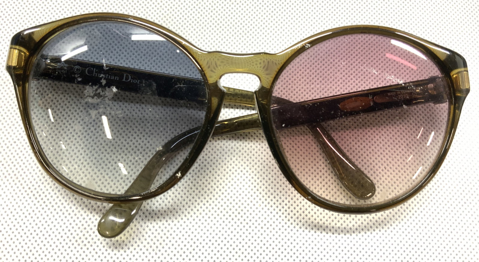CHRISTIAN DIOR Olive Green Sunglasses: Marked on arms Christian Dior. Appears to have purple and blue lens Olive green framed sunglasses with 2 x 2.25 inch wide lens. Arms of glasses have black and white acrylic bands with CD affixed. Mode